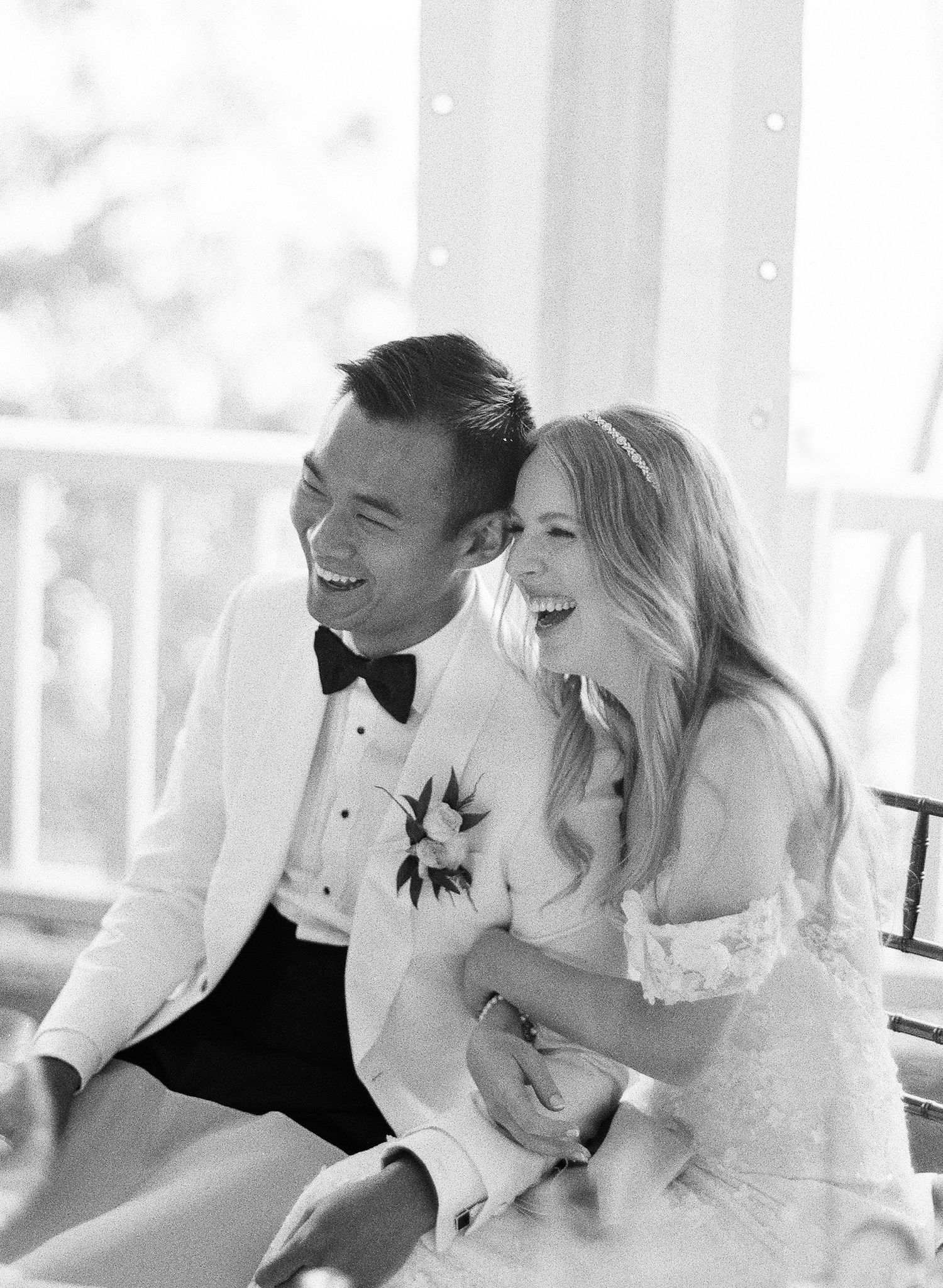 A happy couple shares a candid laughing moment together in black and white wedding attire on their special day.