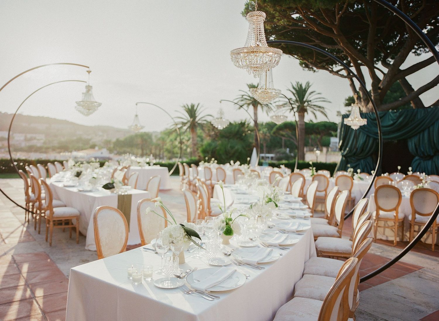 Elegant wedding reception tables set with white linens and crystal chandeliers in an oceanfront venue.