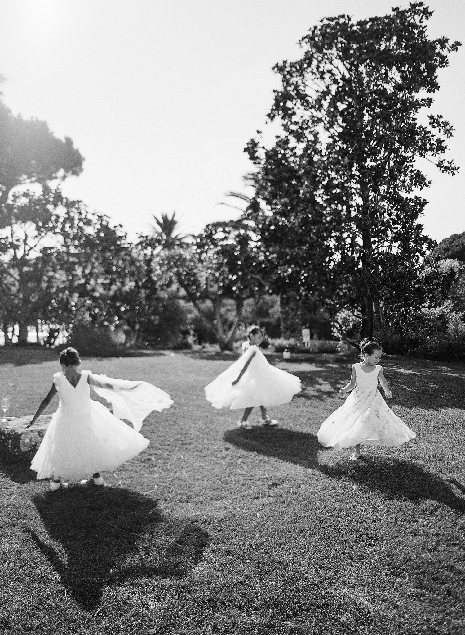 A flowing white wedding dress billows dramatically in the wind across a grassy hillside in a black and white photograph series.