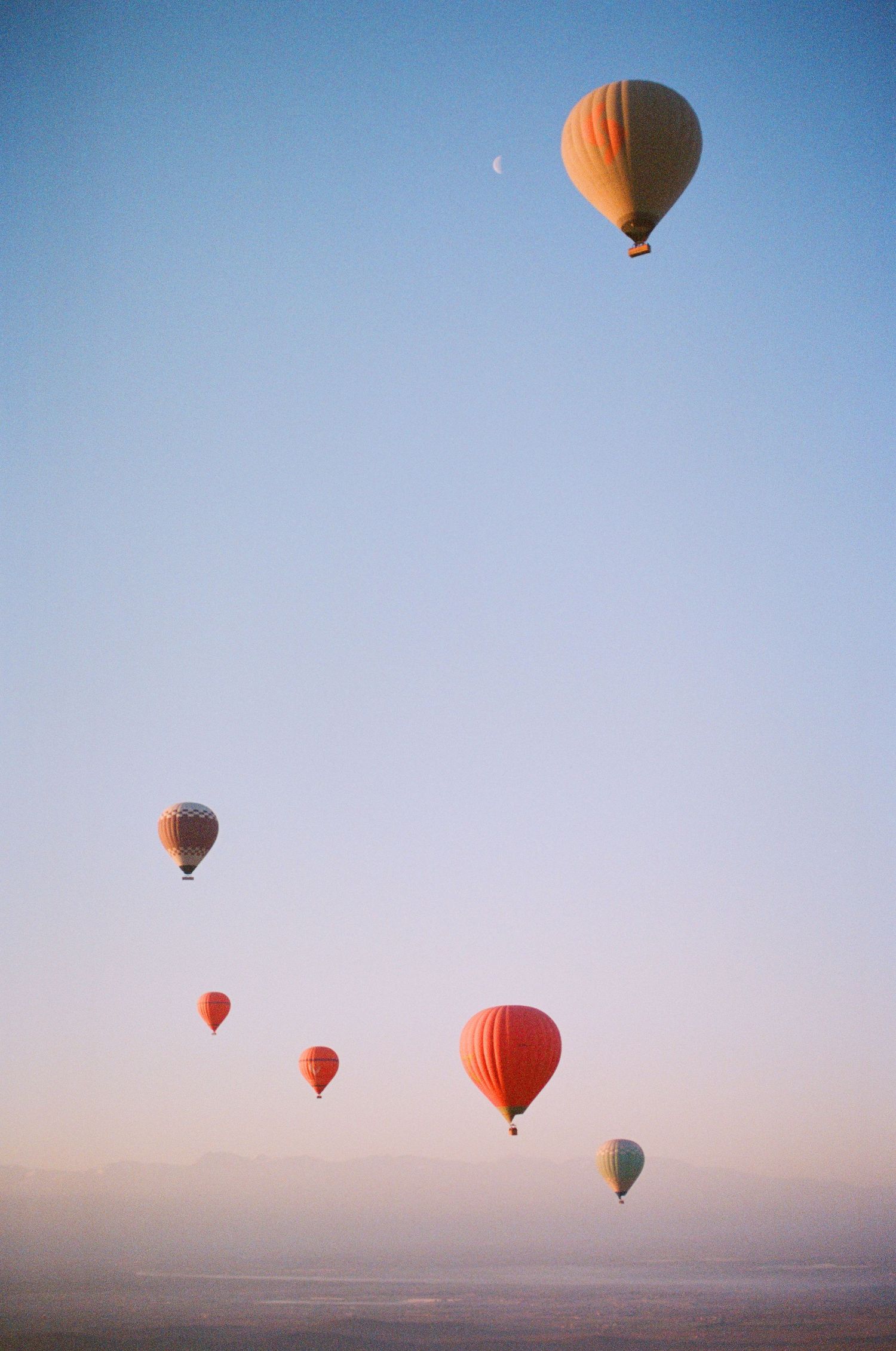 Hot air balloons float gracefully against a soft blue sky during a peaceful sunrise flight over the desert landscape.