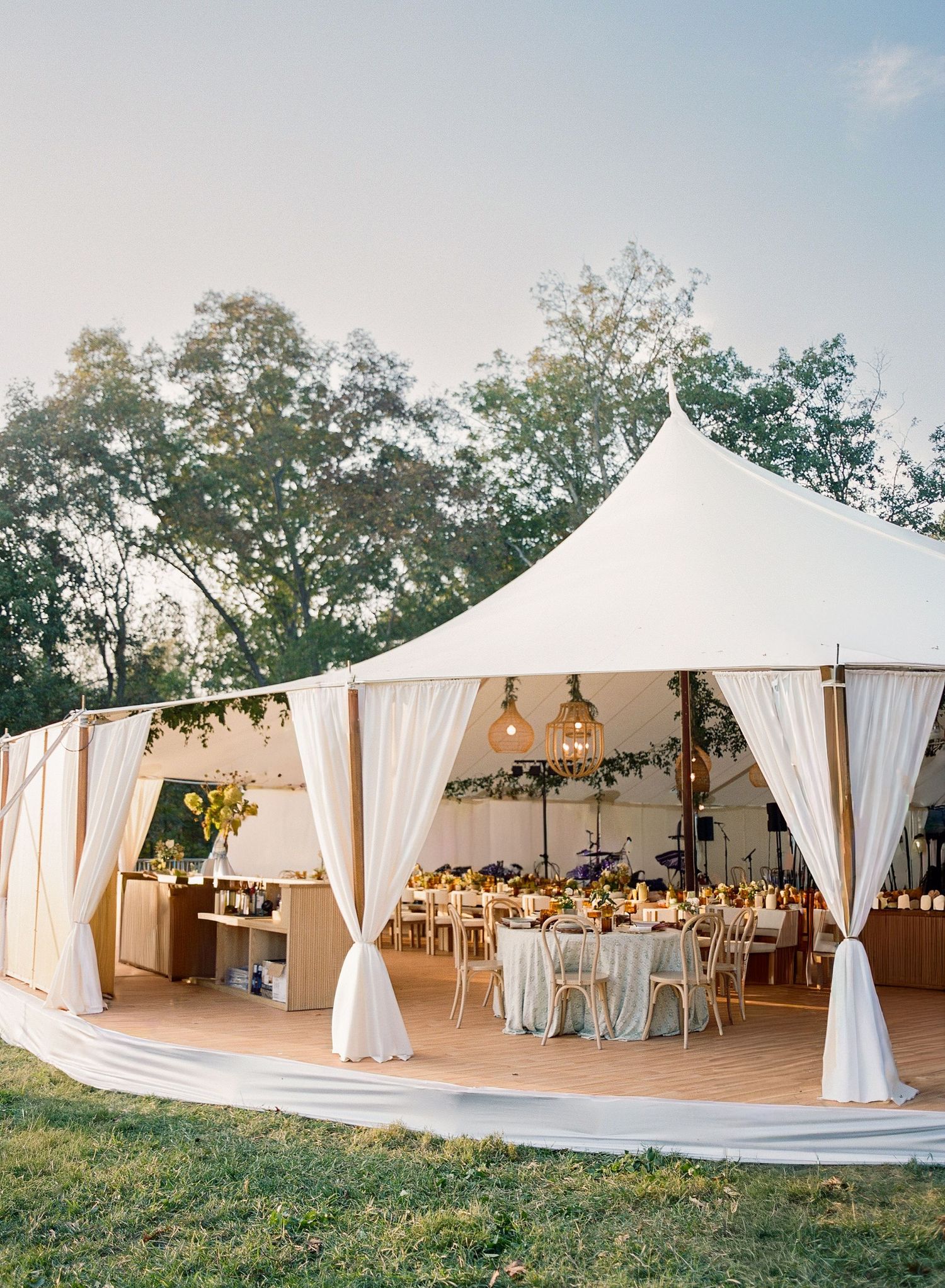 Elegant white wedding tent reception setup with flowing drapes and round tables in an outdoor garden setting.