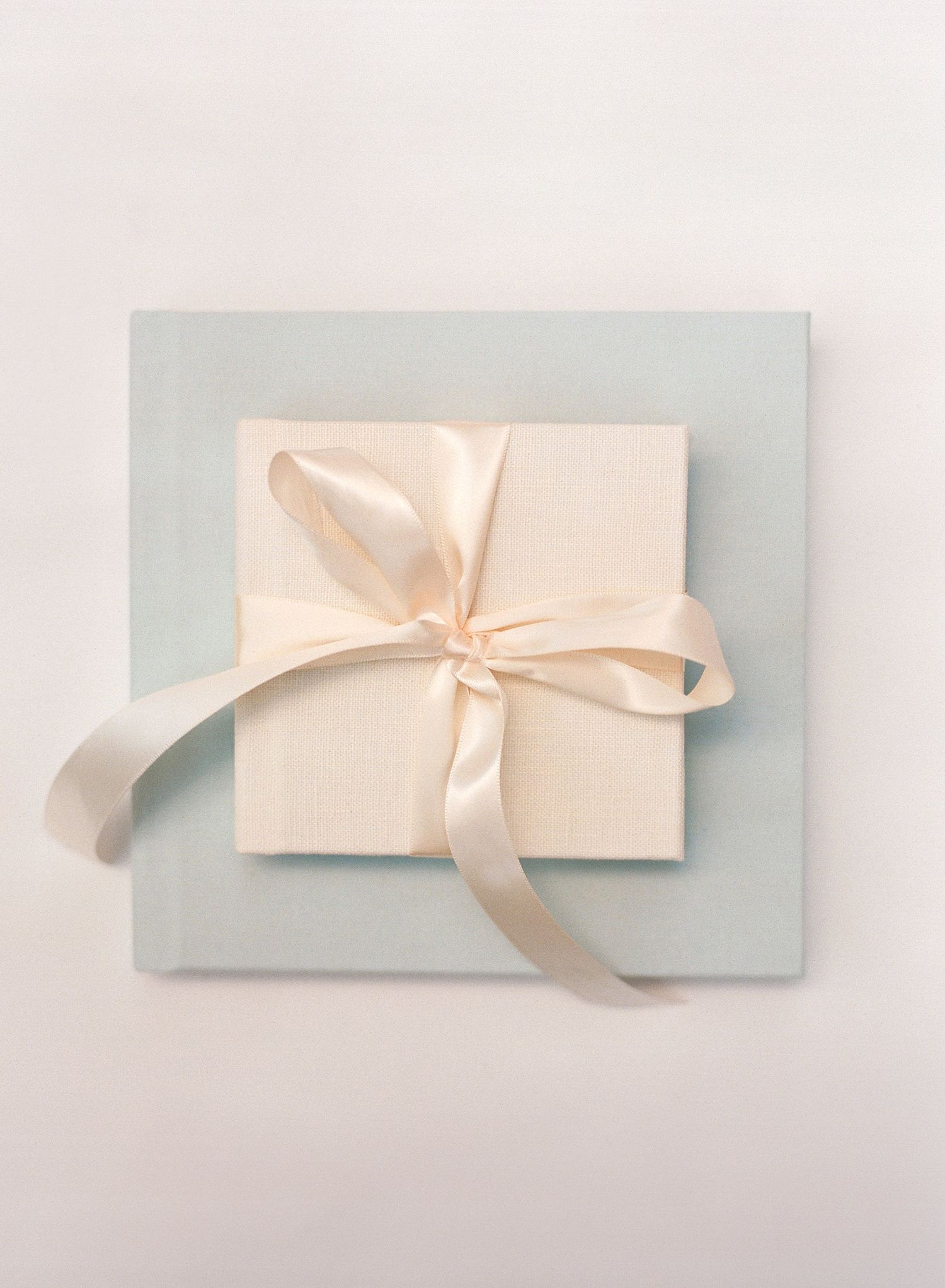White gift box with satin ribbon bow on pale blue background.