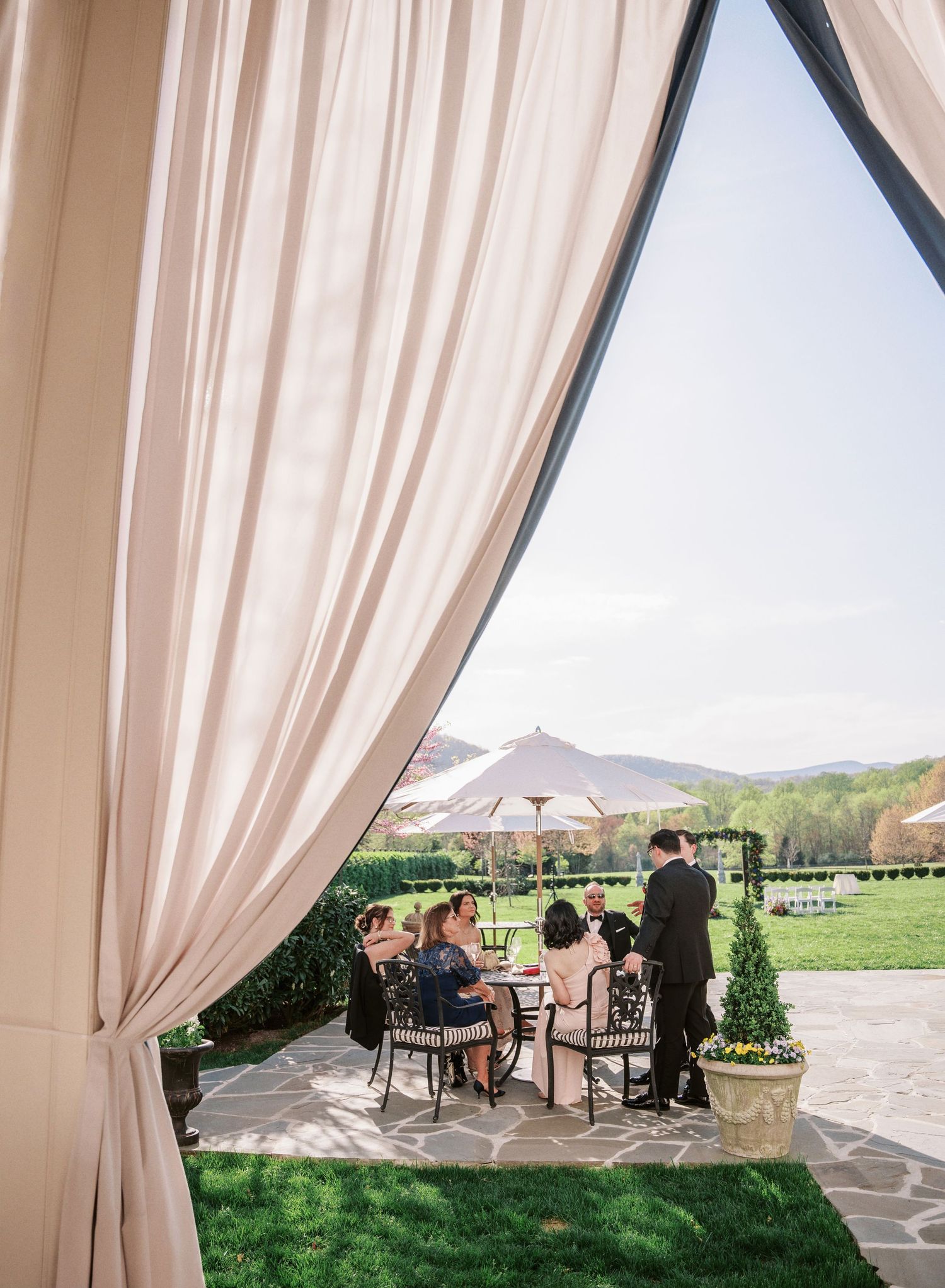 Outdoor wedding reception setup with elegant white drapes framing a scenic mountain view and guests seated at tables.