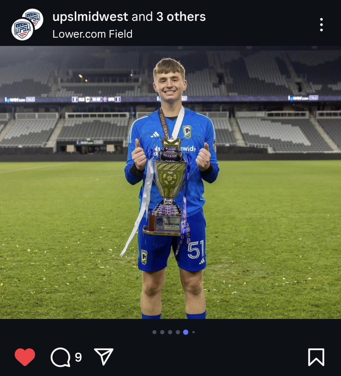 Soccer player on empty field holding championship trophy at Lower.com Field.