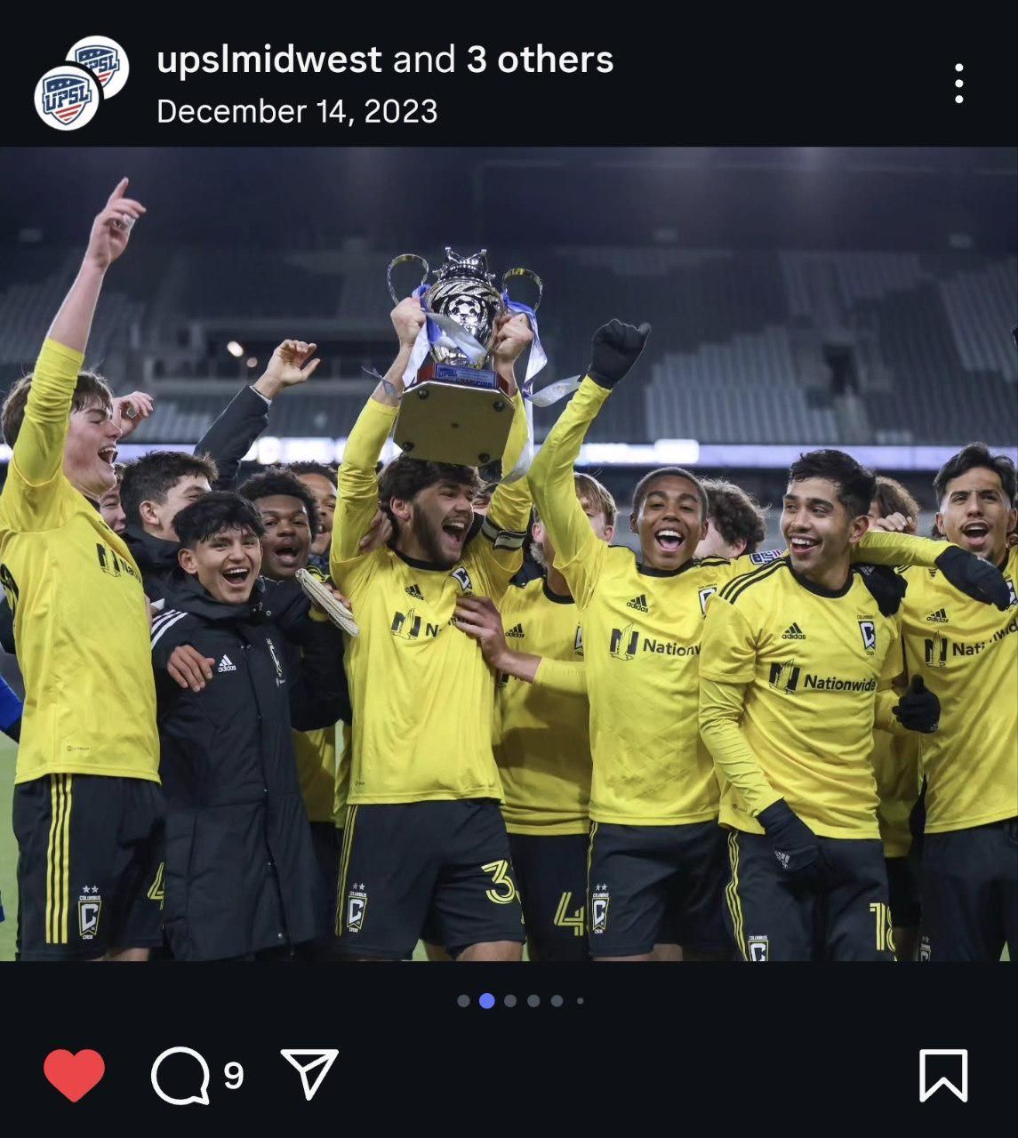 Soccer team in yellow uniforms celebrating with a trophy during nighttime.