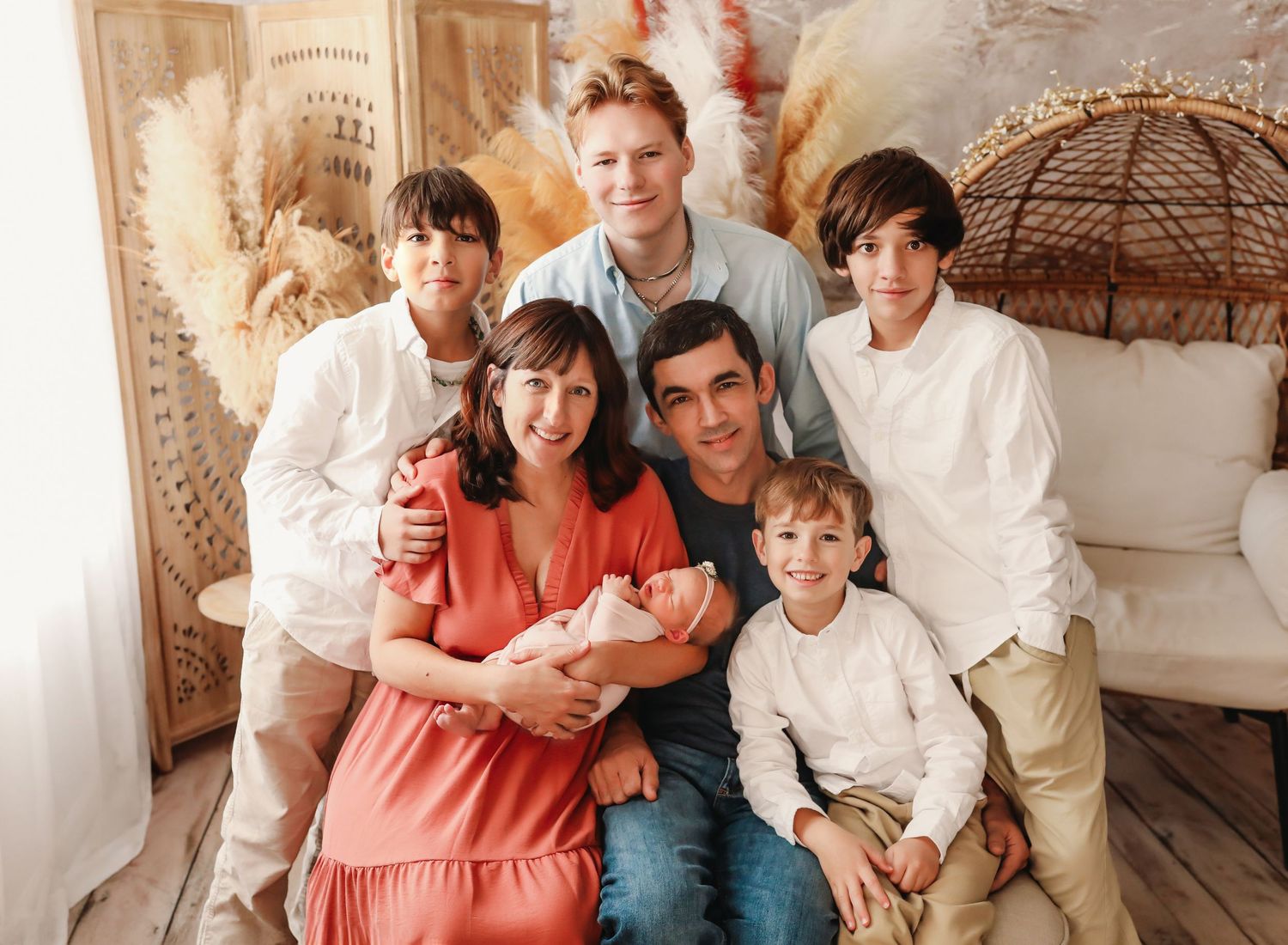 A family in coordinated coral and blue outfits sits together on a couch for a portrait session.