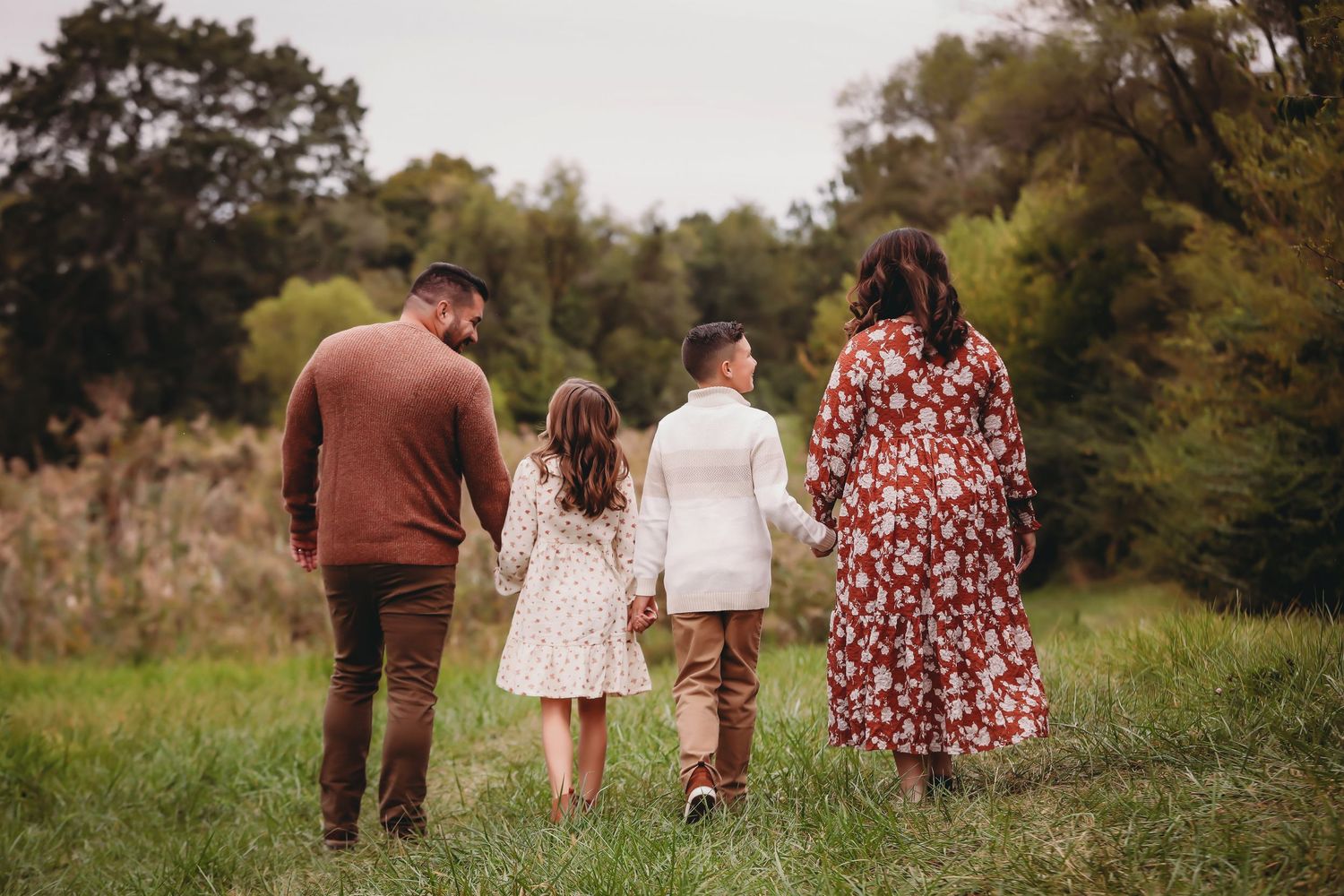 A family walks together hand in hand through a lush green field during golden hour.