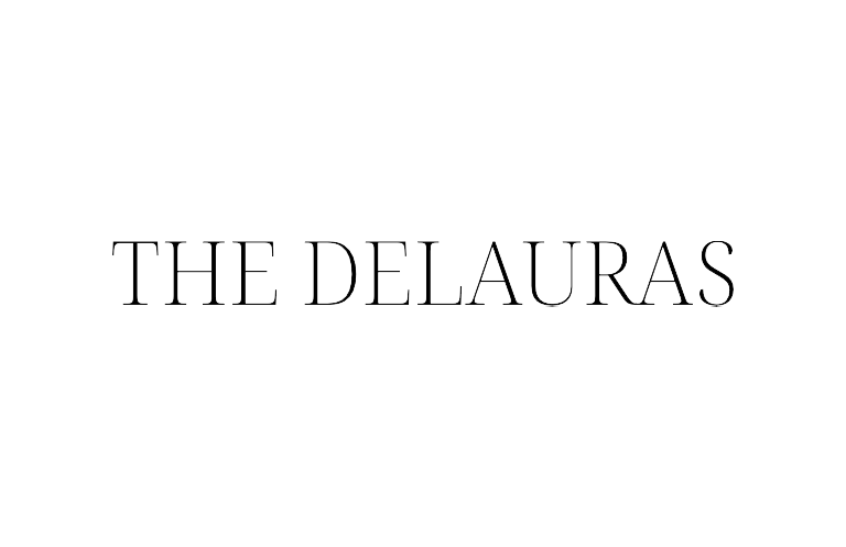 A stylish white text logo reading 'THE DELAURAS' in an elegant serif font on a plain background.