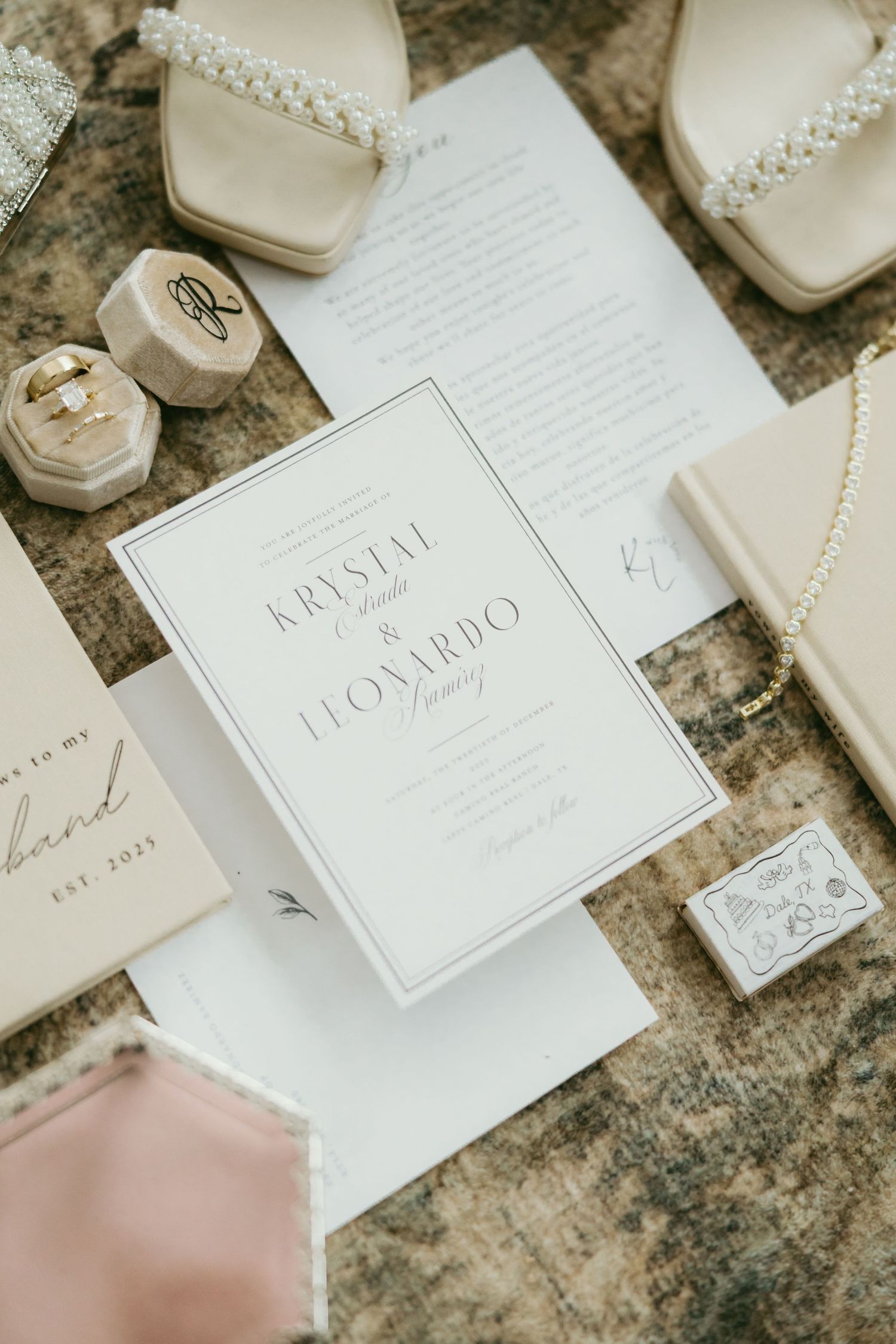 Elegant wedding invitation suite for Krystal and Leonardo displayed with pearl heels, ring boxes, and blush accessories.