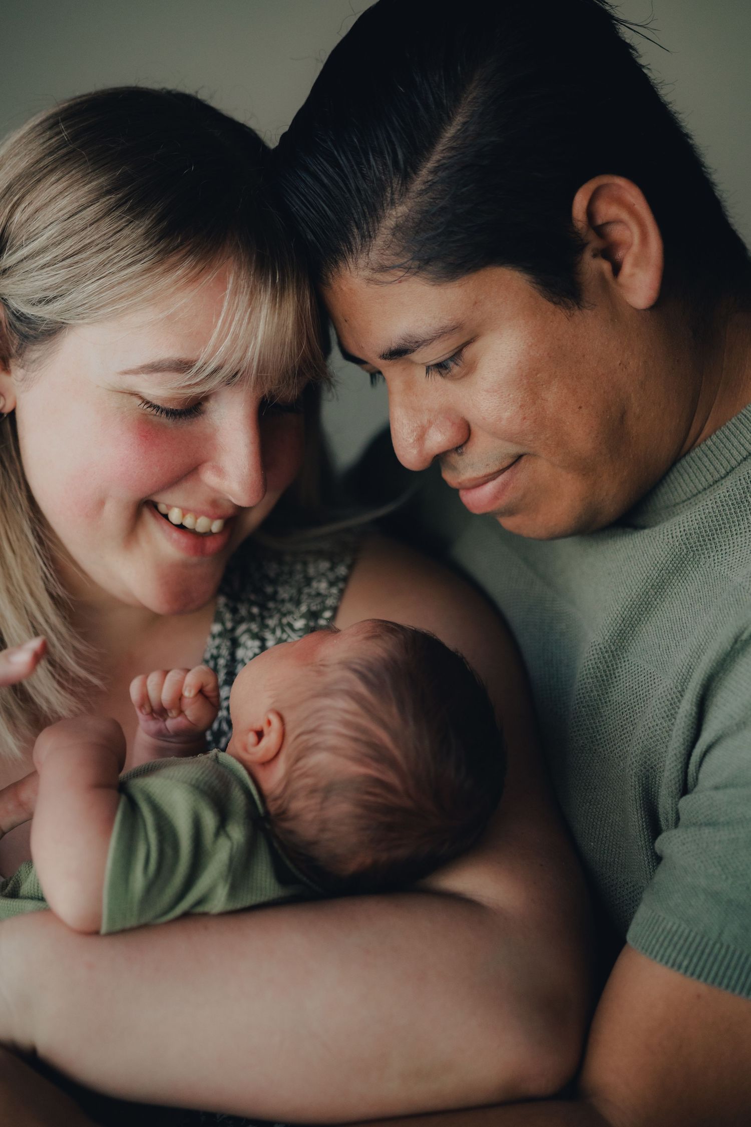 Happy couple smiling at their newborn baby, tender family portrait with parents cradling infant.