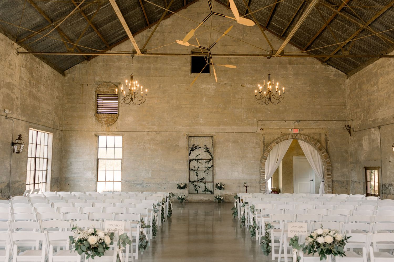 Warehouse chapel interior with wooden beams, chandeliers and white ceremony chairs.