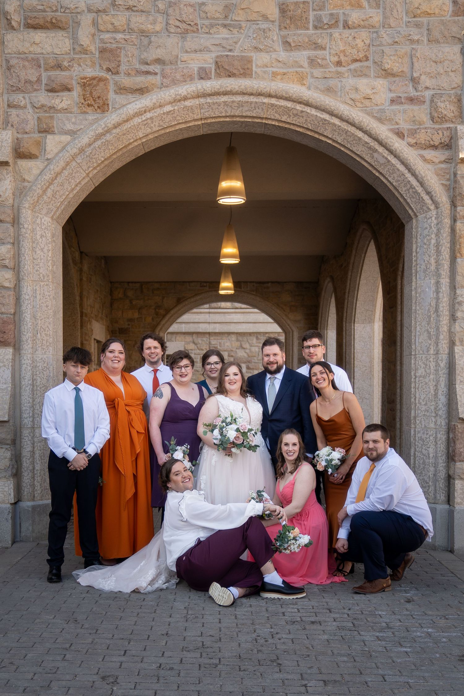 Wedding party poses together under stone archways at sunset with warm lighting.