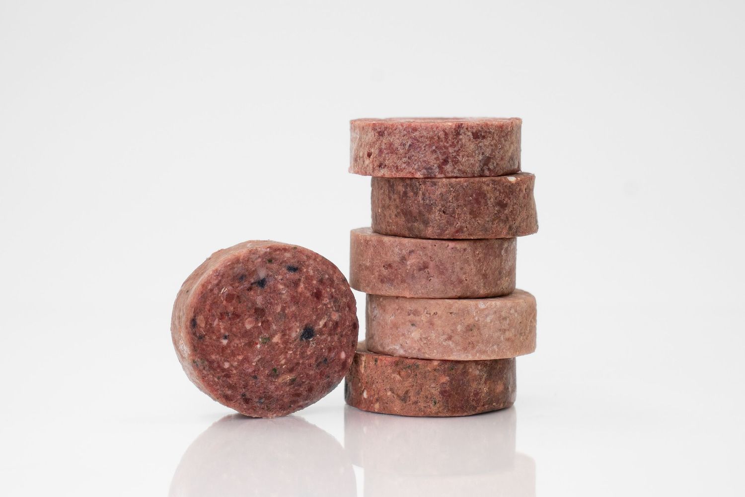 Frozen raw dog food stacked in different arrangements against a white background.