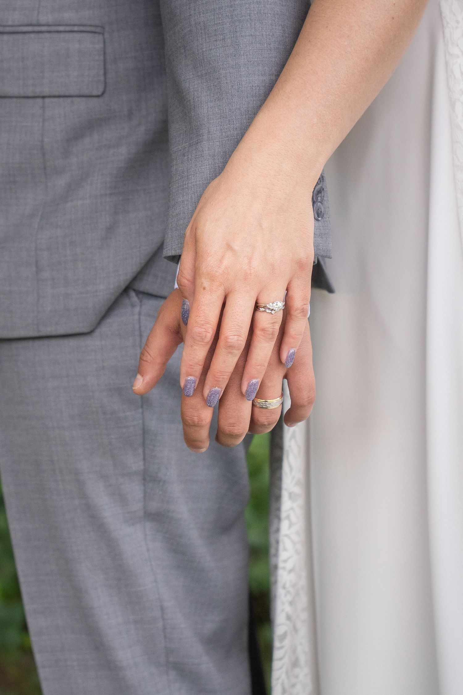 Close-up view of hands wearing silver engagement and wedding rings against a gray and white background.