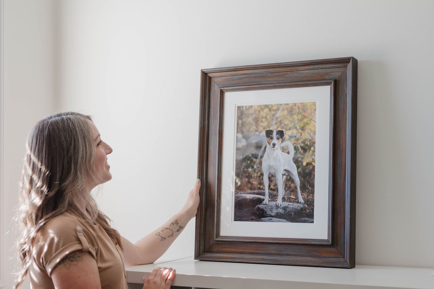 A person hangs framed artwork on a white wall while arranging a gallery wall display.