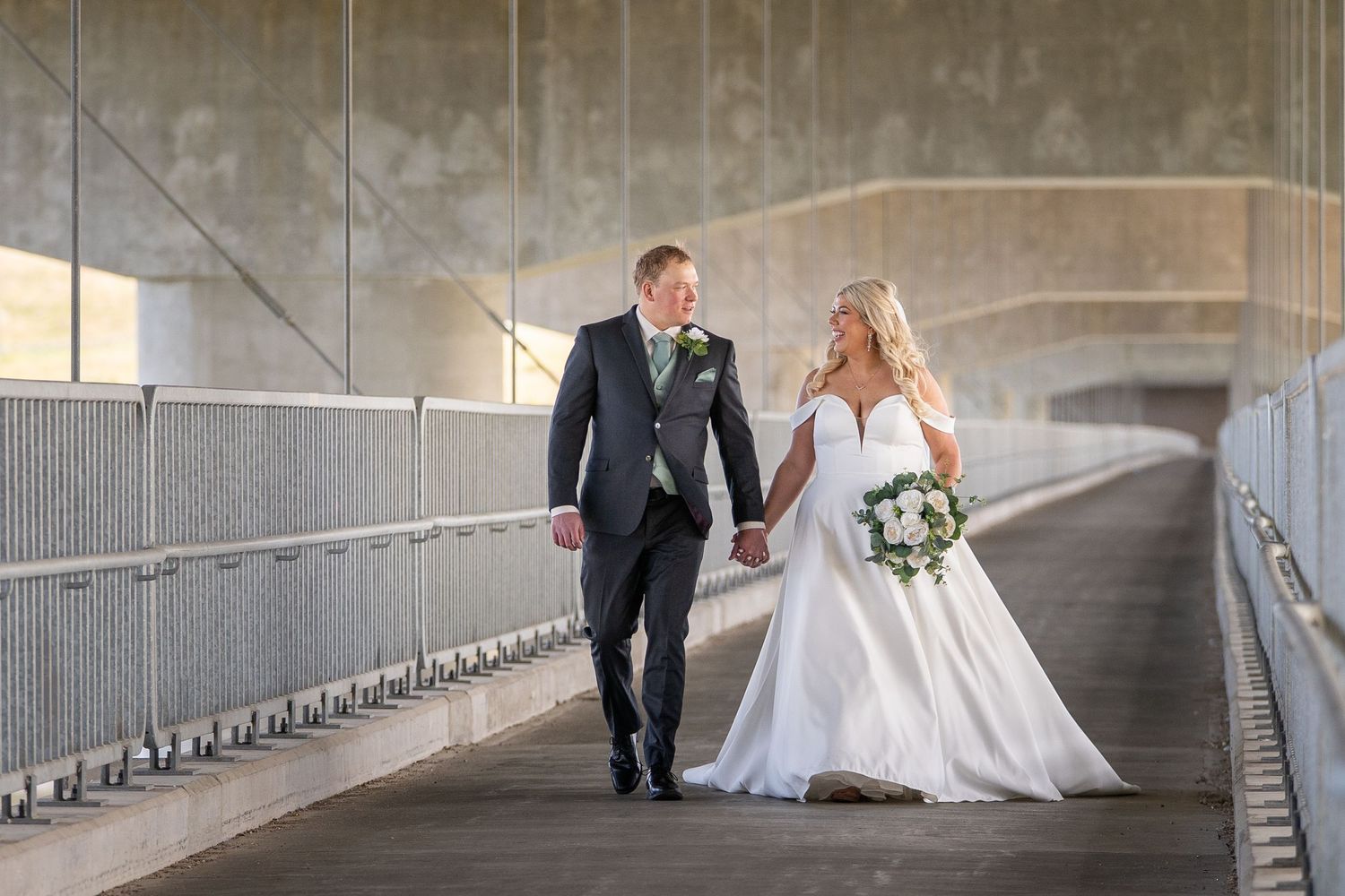 Wedding couple walks through a modern concrete tunnel with dramatic lighting and shadows creating a romantic atmosphere.