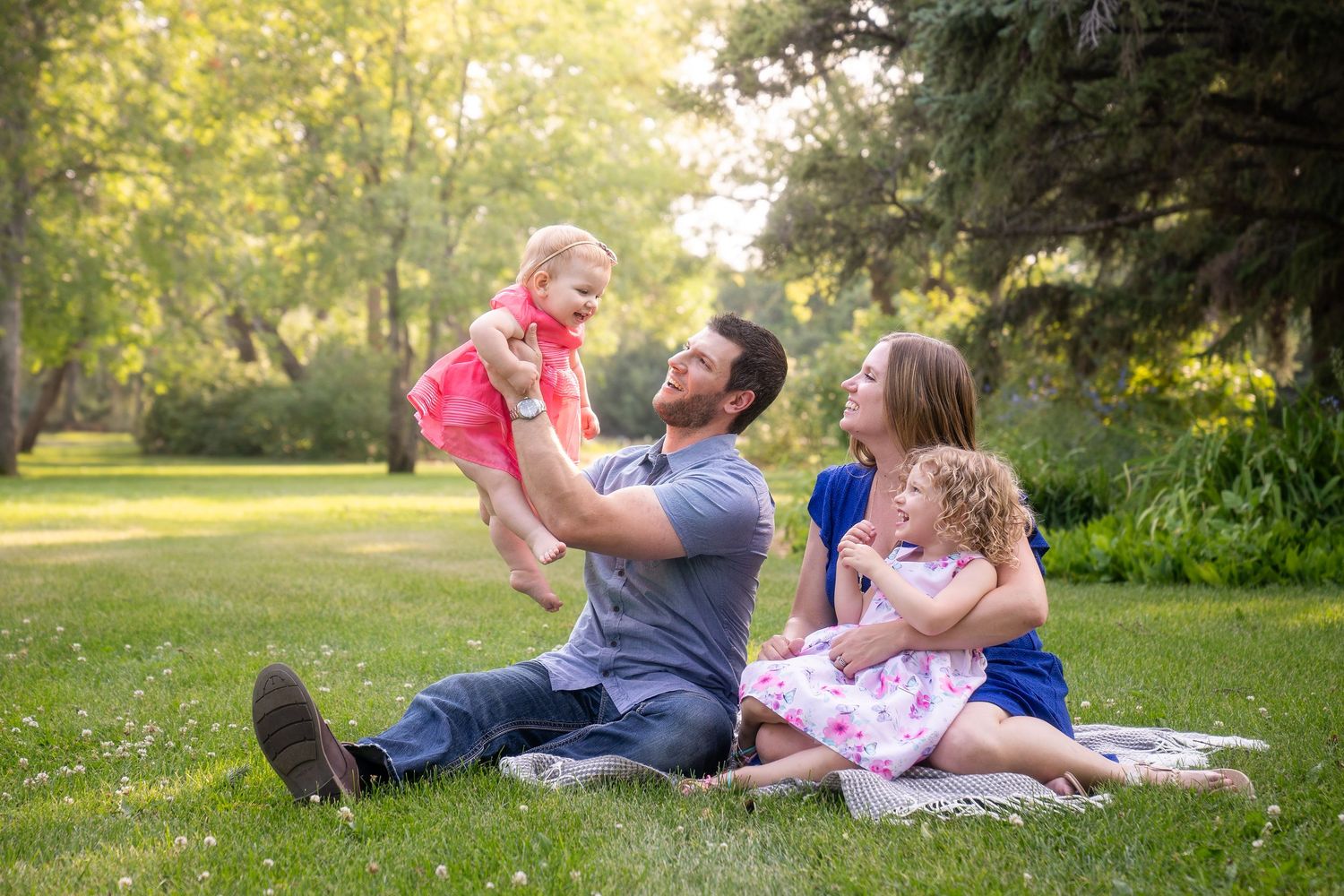 Family enjoying a relaxing afternoon together on a blanket in a sunlit park during summer.