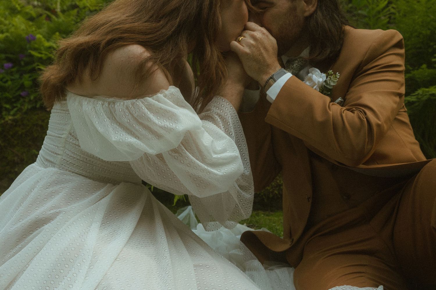 A couple in wedding attire embraces romantically in a lush green outdoor setting during their special day.