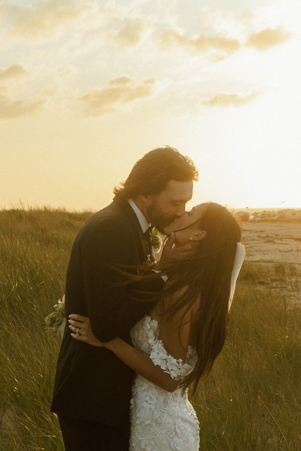 Couple embracing in golden sunset light among tall grass. Cape Cod Micro Wedding