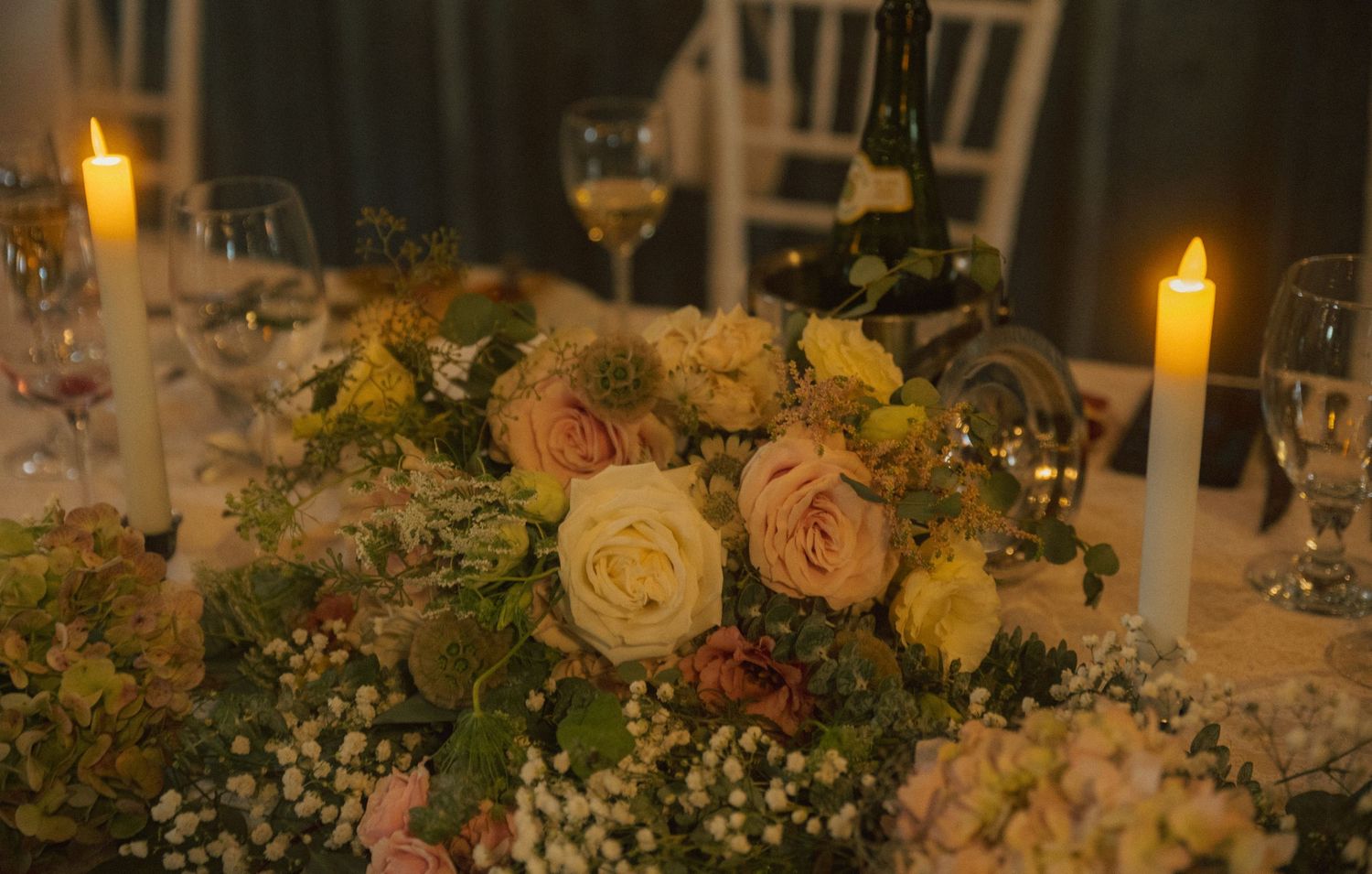 Wedding reception table decorated with blush roses, baby's breath and glowing taper candles.