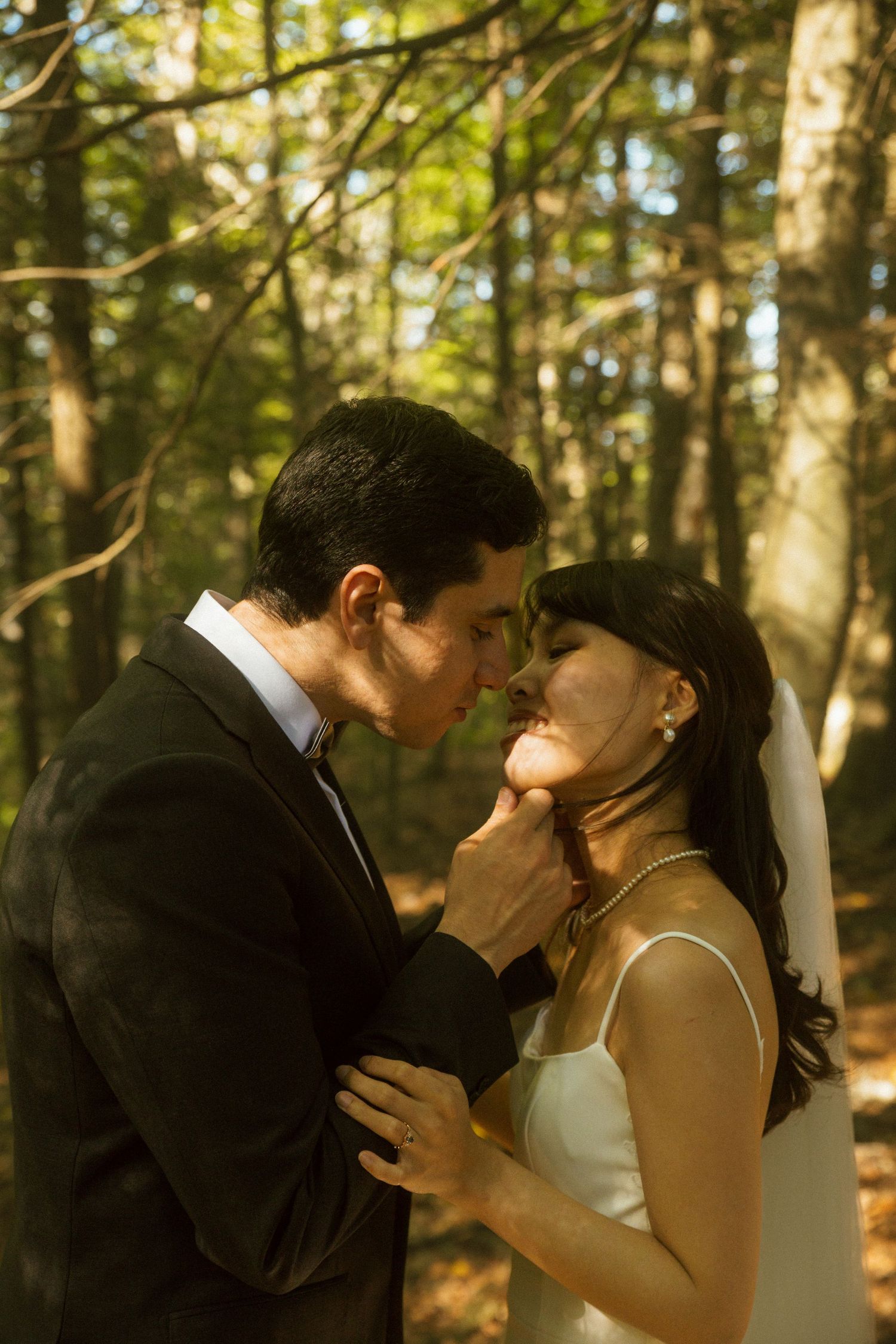 A romantic wedding couple share an intimate moment in a sunlit forest setting.