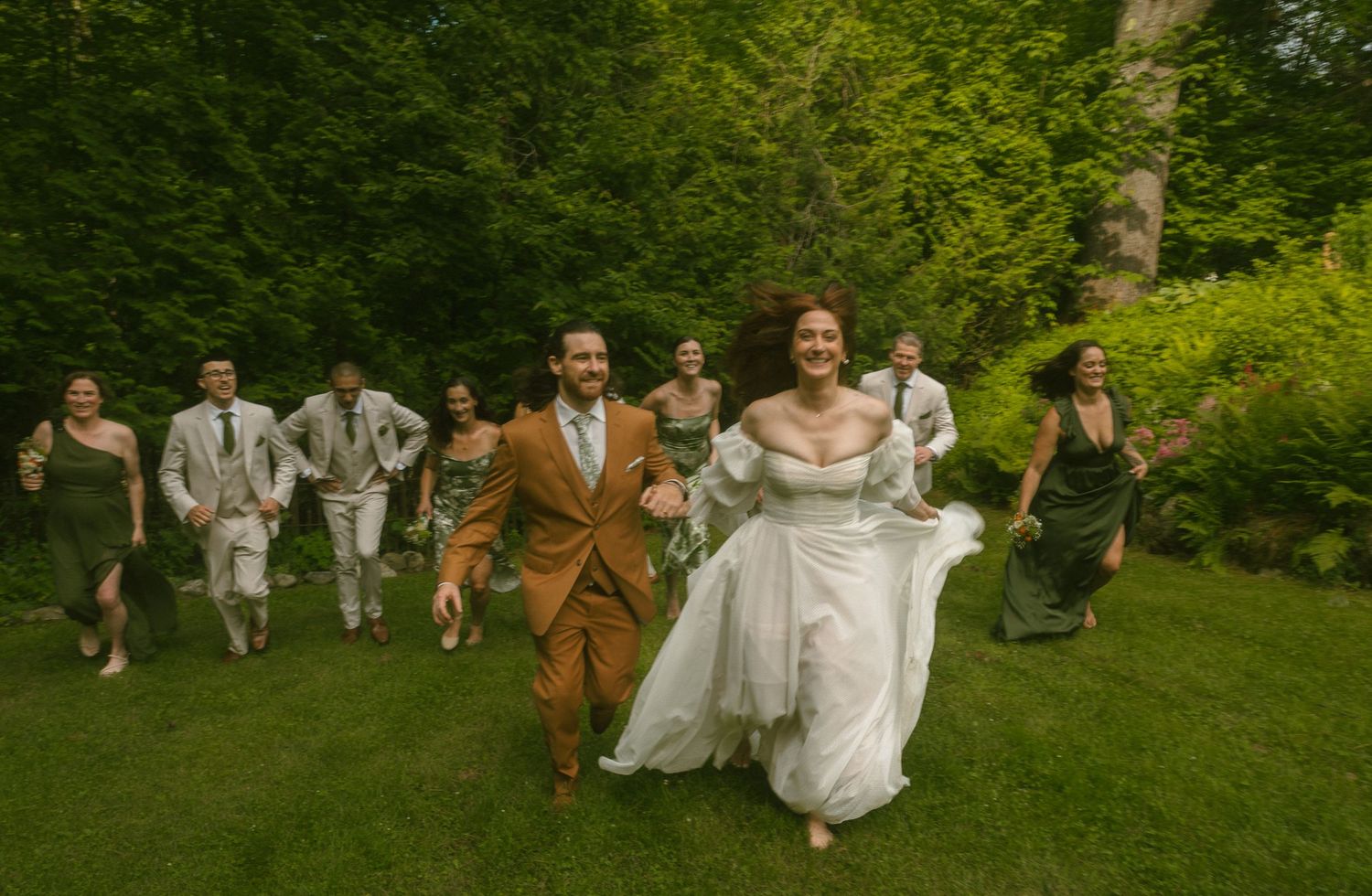 Wedding celebration in a verdant garden with people running joyfully through the grounds.