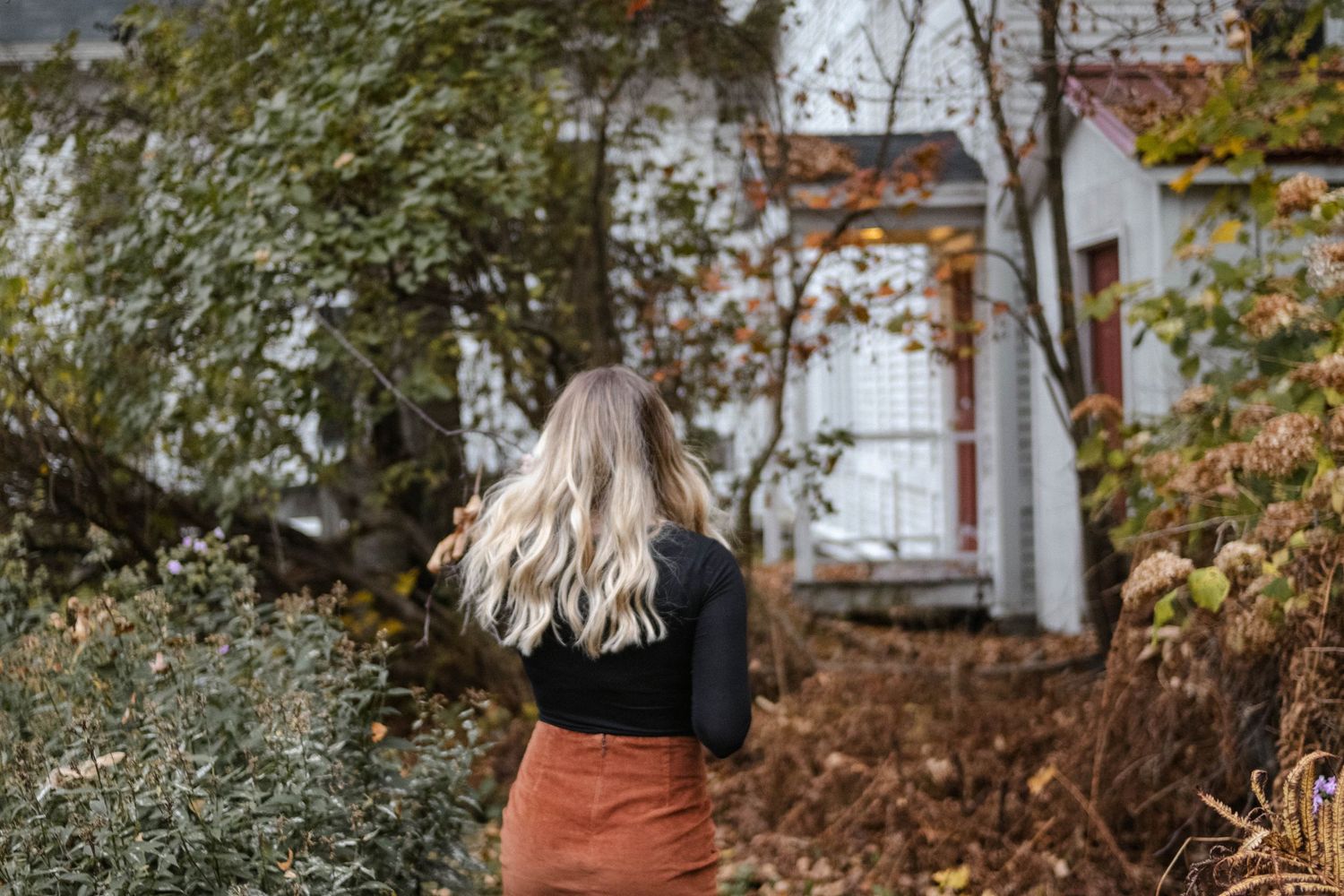 Autumn garden scene with rustic decor and pumpkins arranged on wooden steps leading to a white house.