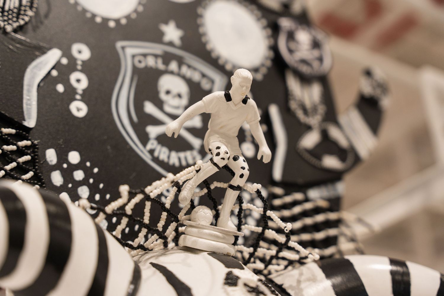 Black and white soccer player figurine displayed on Orlando Pirates themed fabric decoration.