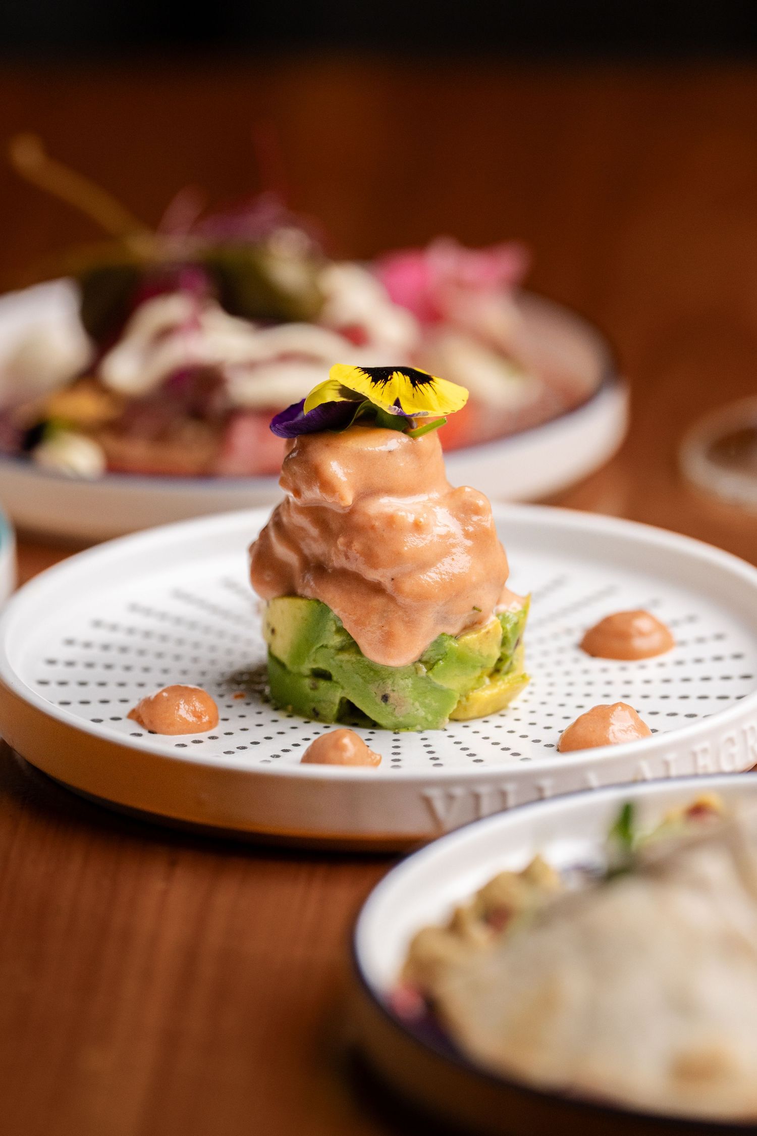 Elegant salmon tartare on avocado, topped with edible flowers on a white textured plate at a fine dining restaurant.