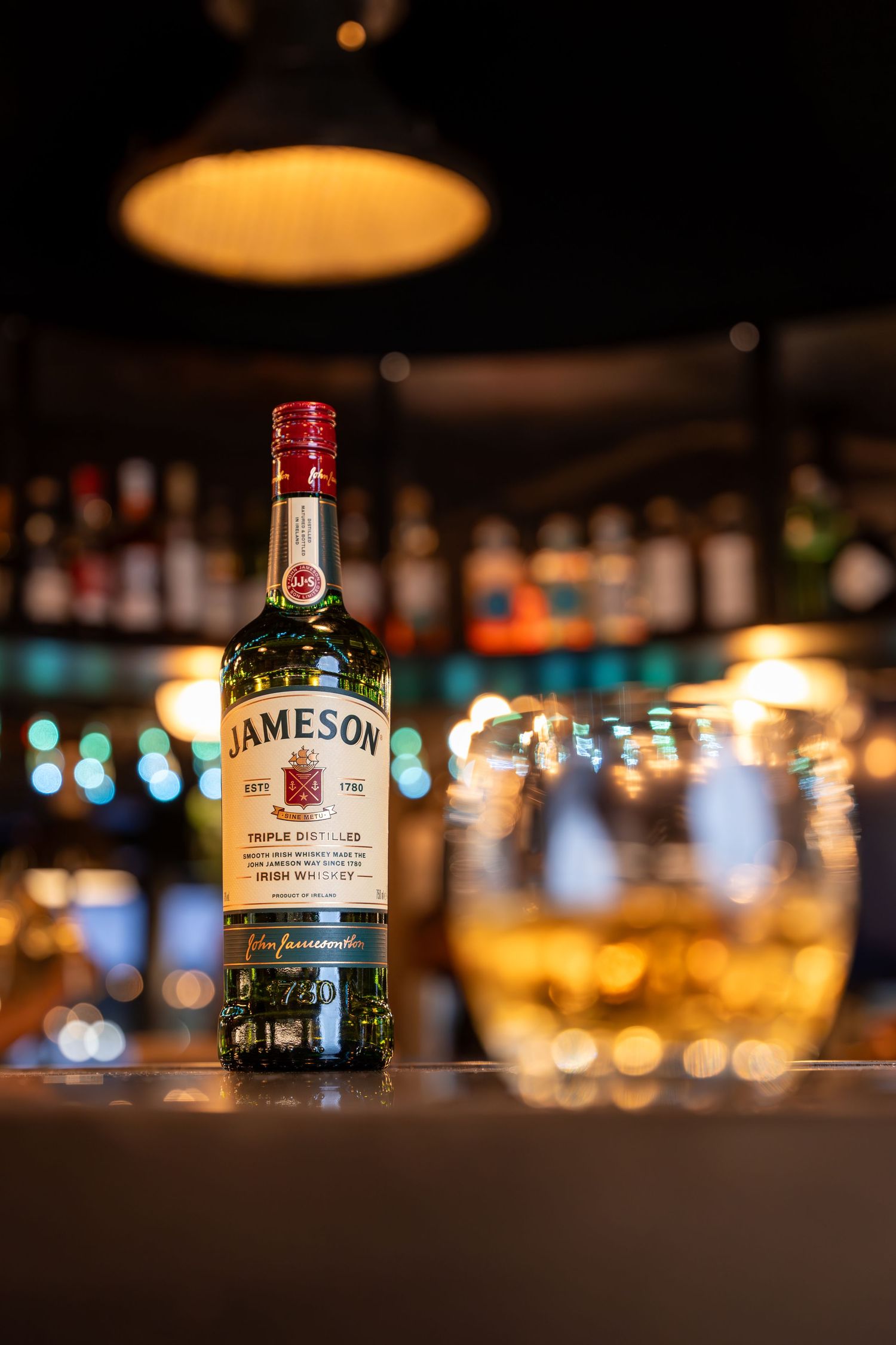 Bottle of Jameson Triple Distilled Irish Whiskey on a bar counter with a whiskey glass.