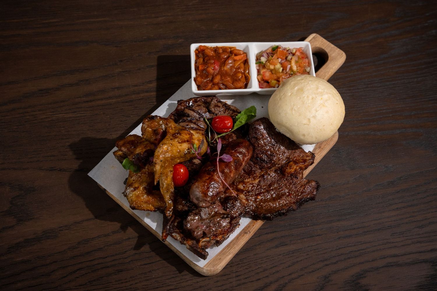 Grilled meat platter with ugali, chicken wings, and two sauces served on a wooden board.