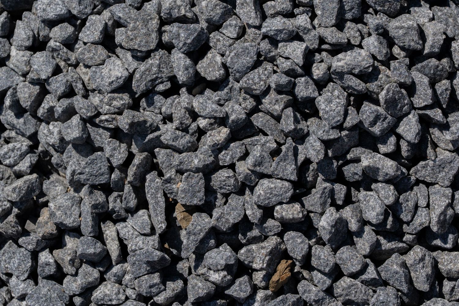 Close-up of dark grey crushed stone gravel aggregate texture background.