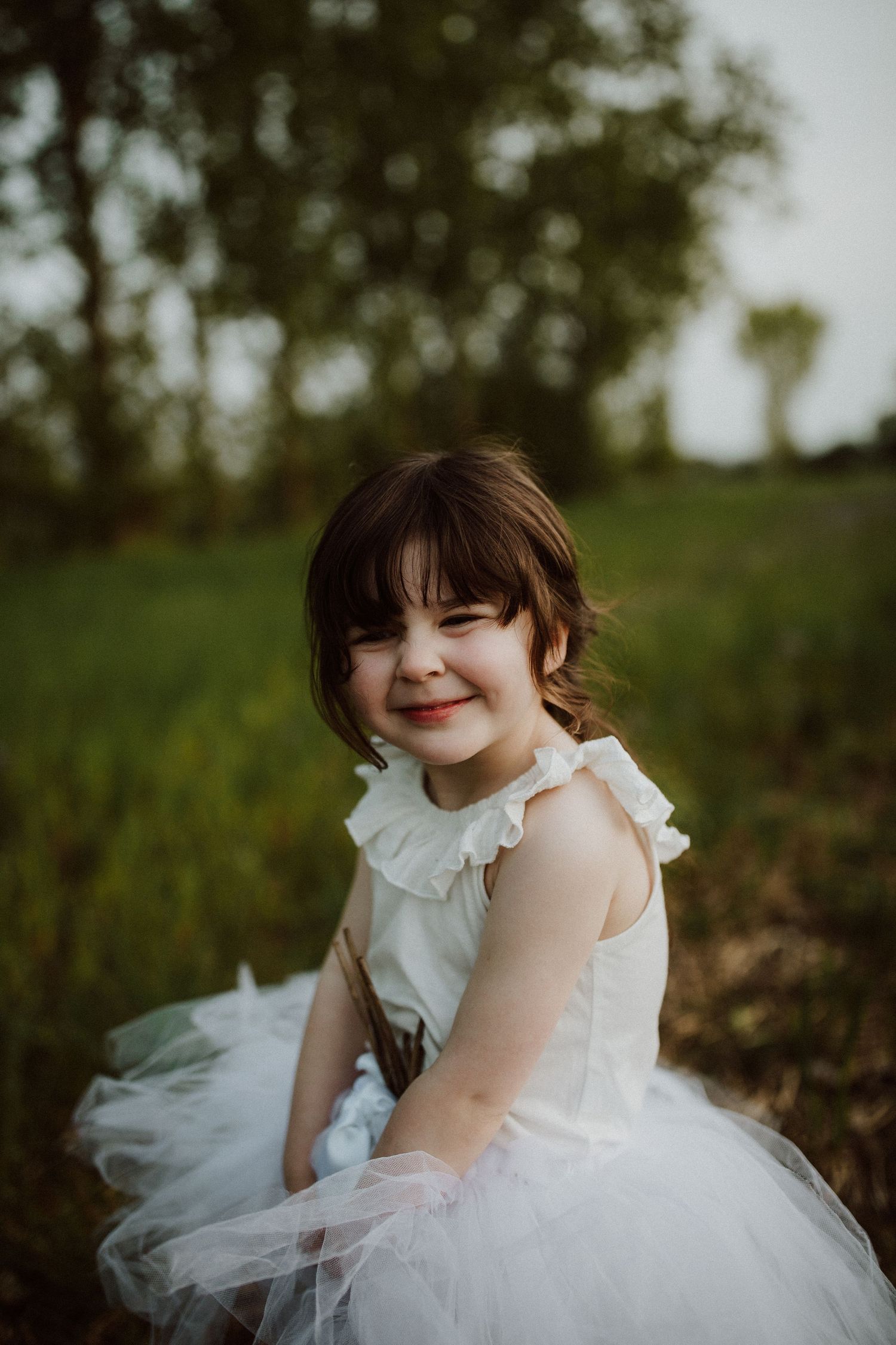 Young child in white tulle dress smiles during outdoor portrait session.