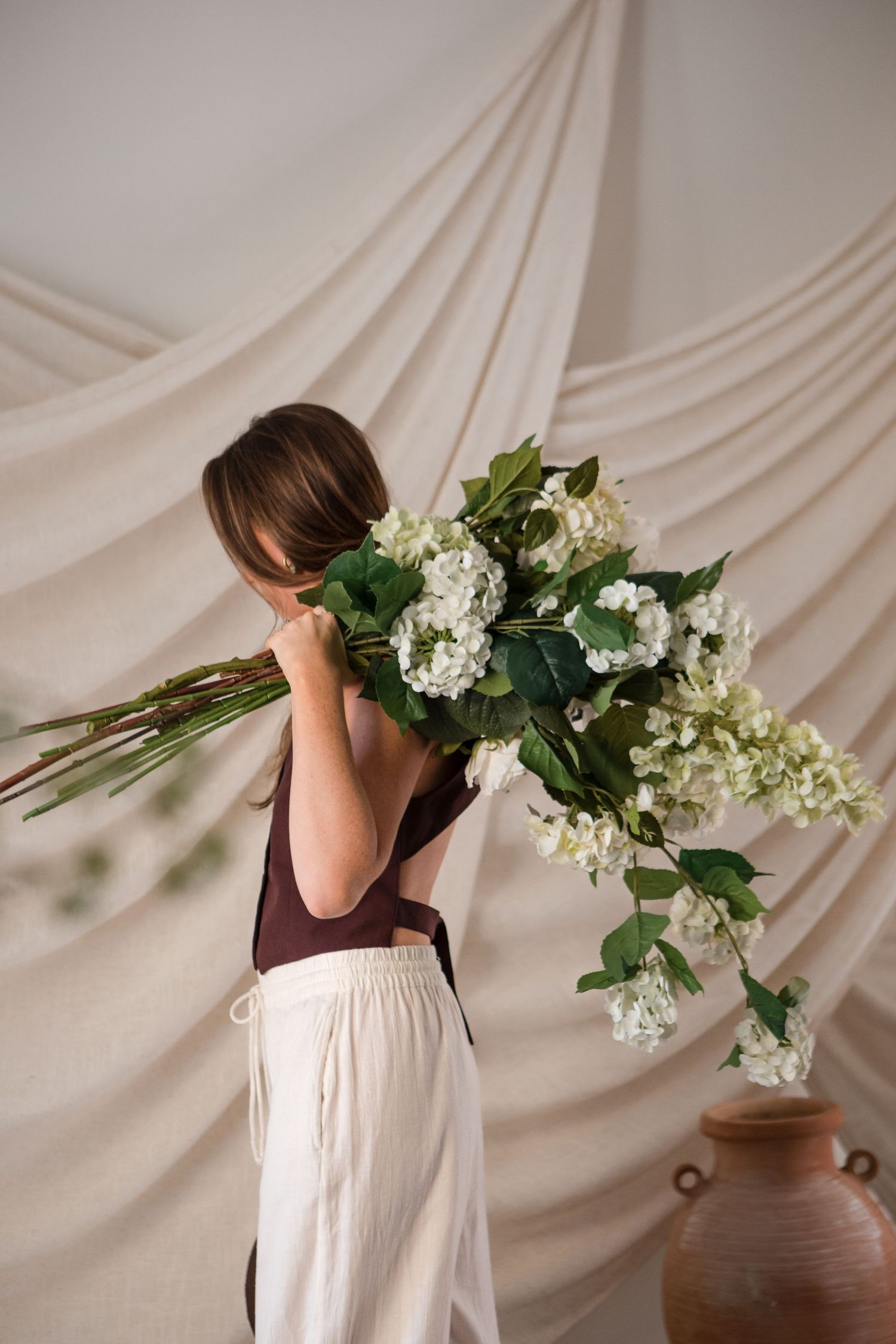 A series of five artistic photographs showing white hydrangea flowers against a soft beige draped fabric background.