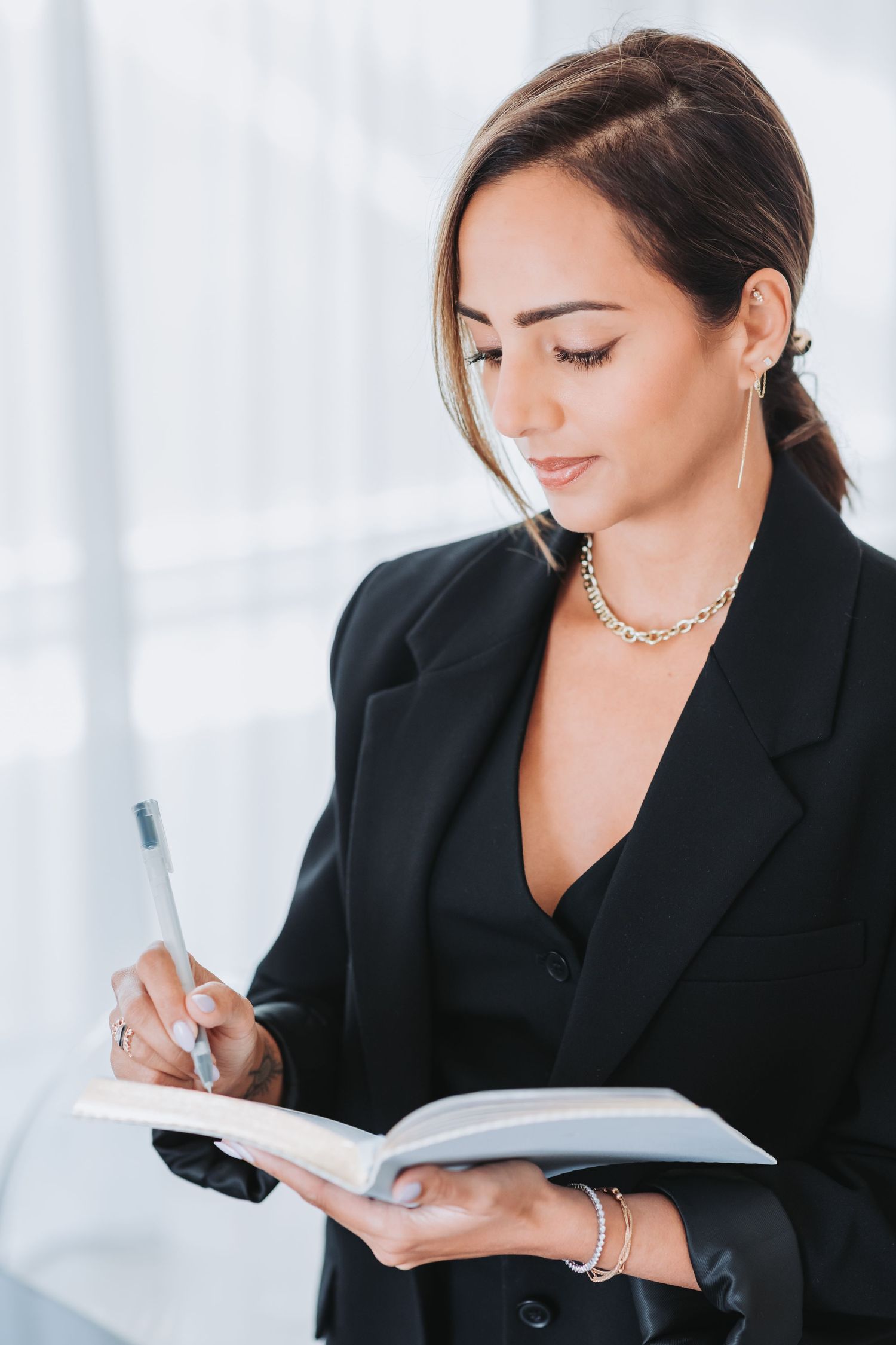Business professional in black blazer writing in notebook at bright office setting.