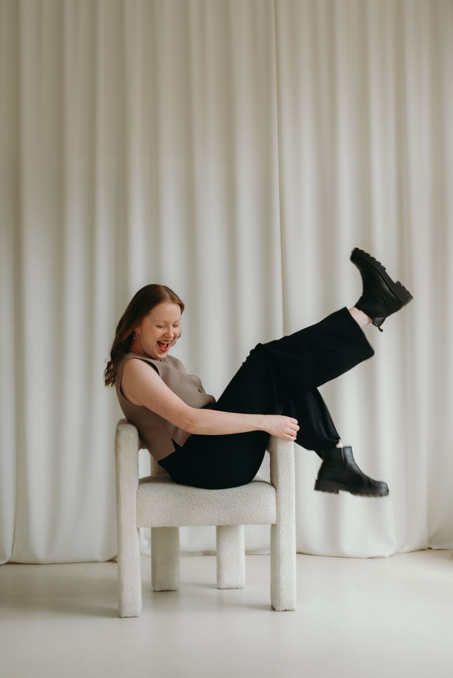 A sequence of artistic photographs showing a figure in black clothing reclining on white chairs against a light curtain backdrop.