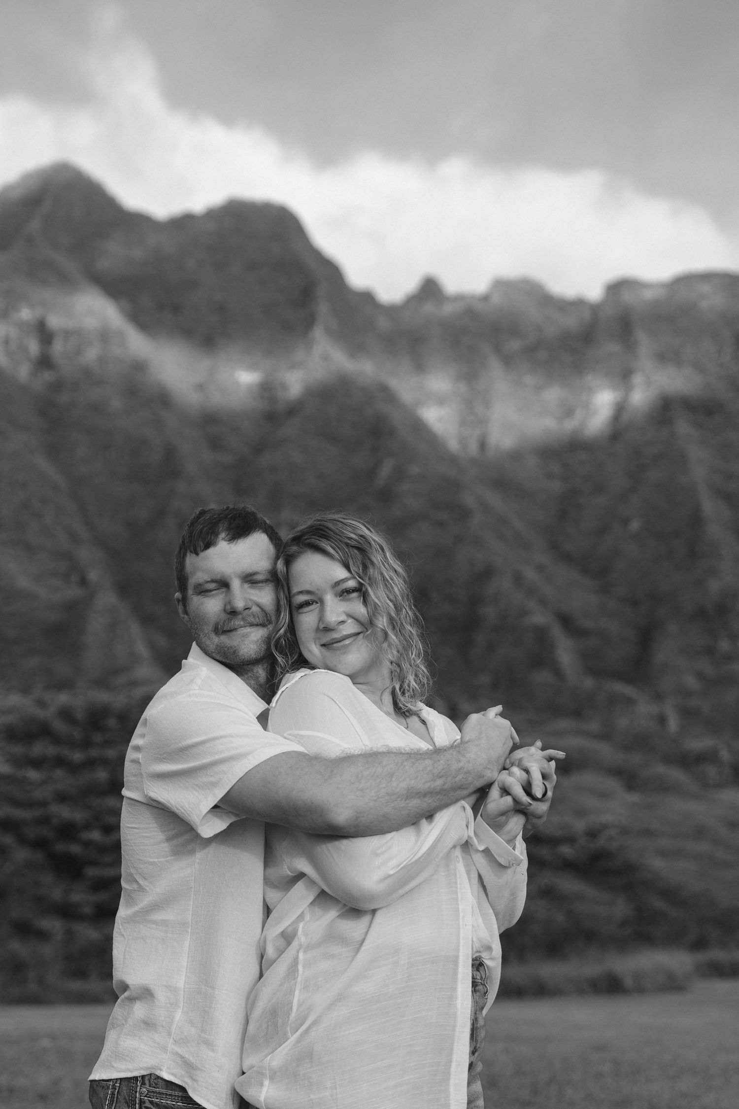 Black and white photo of couple embracing with dramatic mountain peaks behind them.