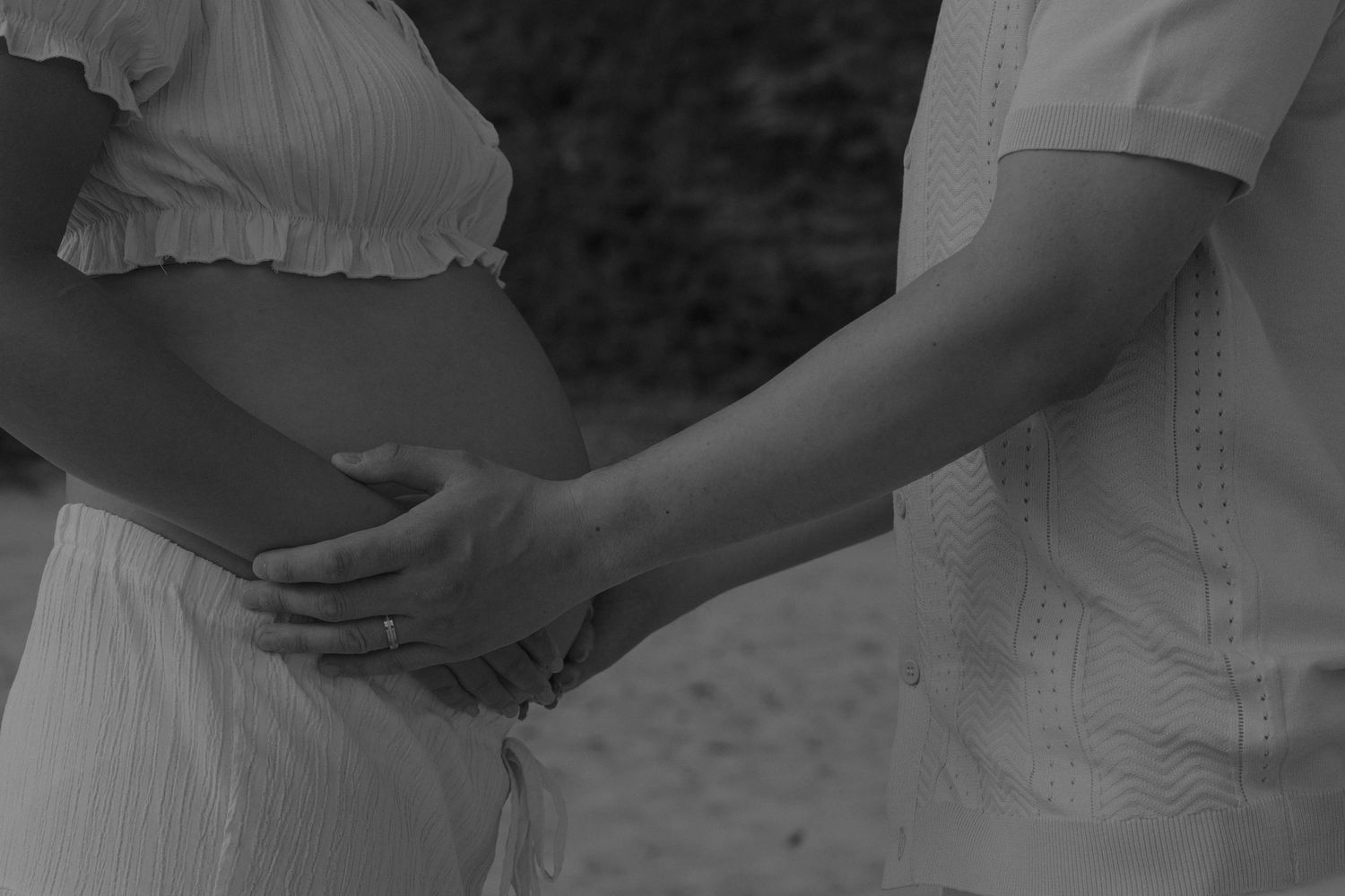 Black and white photo of a pregnant woman and partner holding hands, showcasing a maternity moment.