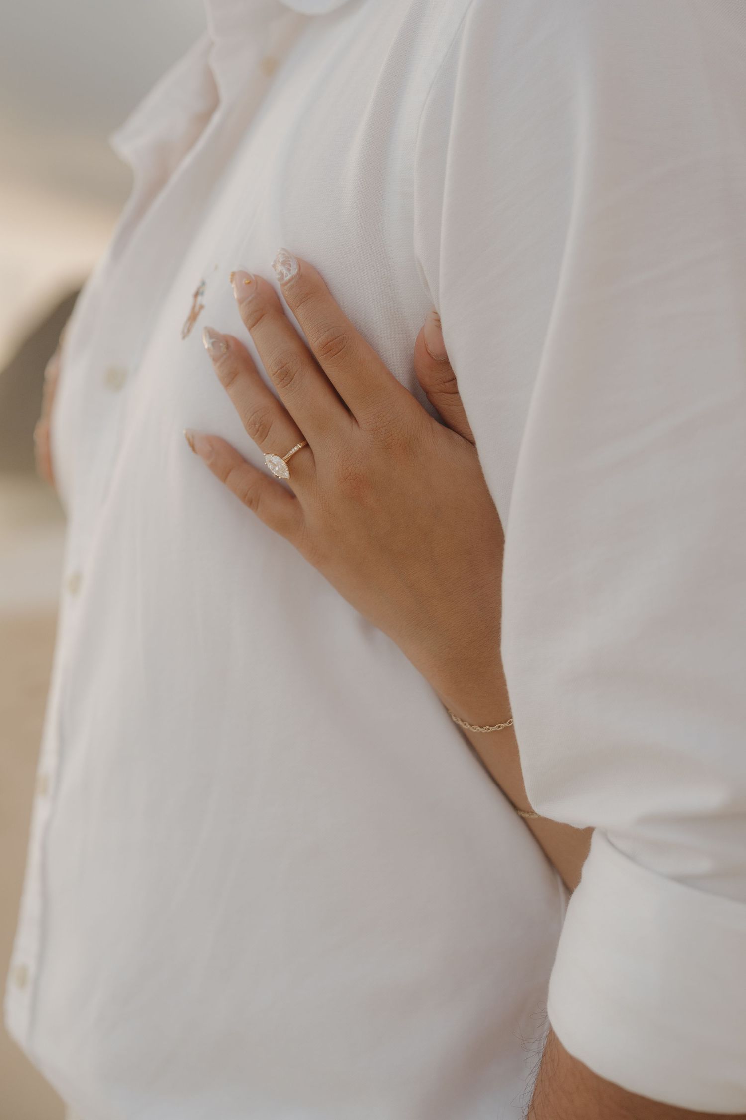 Close-up of a woman's hand with an engagement ring resting on a white button-down shirt.