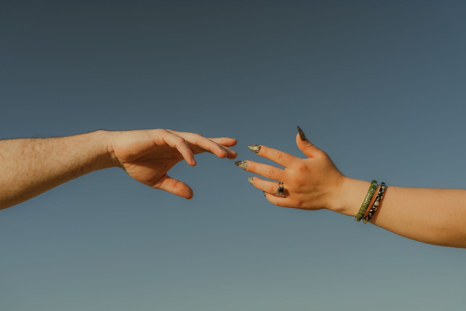 Two hands reaching toward each other against a clear blue sky, symbolizing connection and unity.
