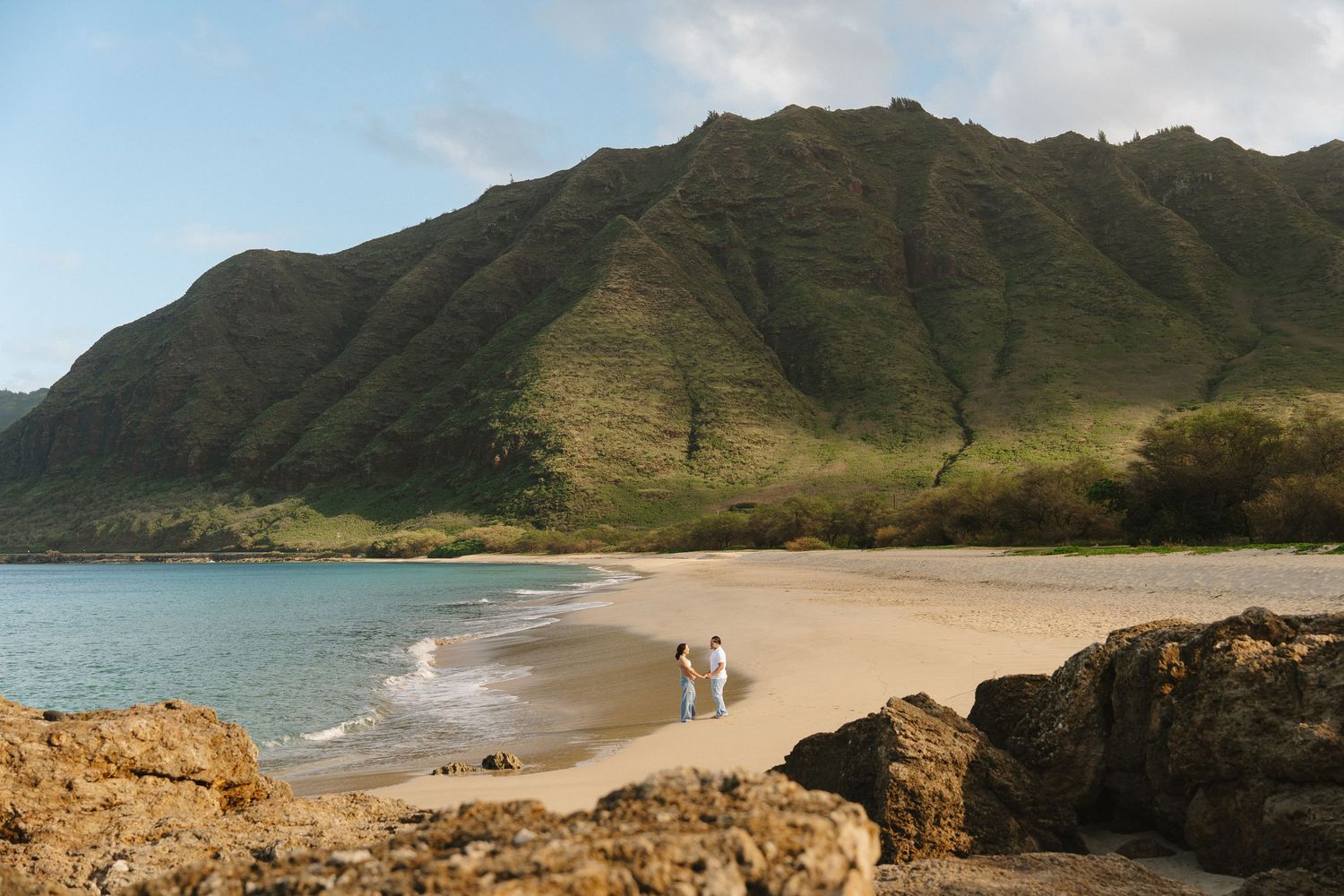 Couple walking on secluded sandy beach surrounded by dramatic green mountains.