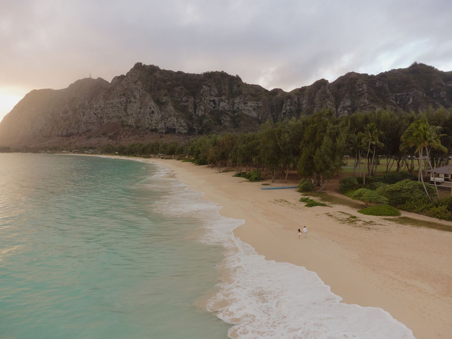 Aerial view of a stunning Hawaiian beach with turquoise waters, white sand, and dramatic mountain backdrop.