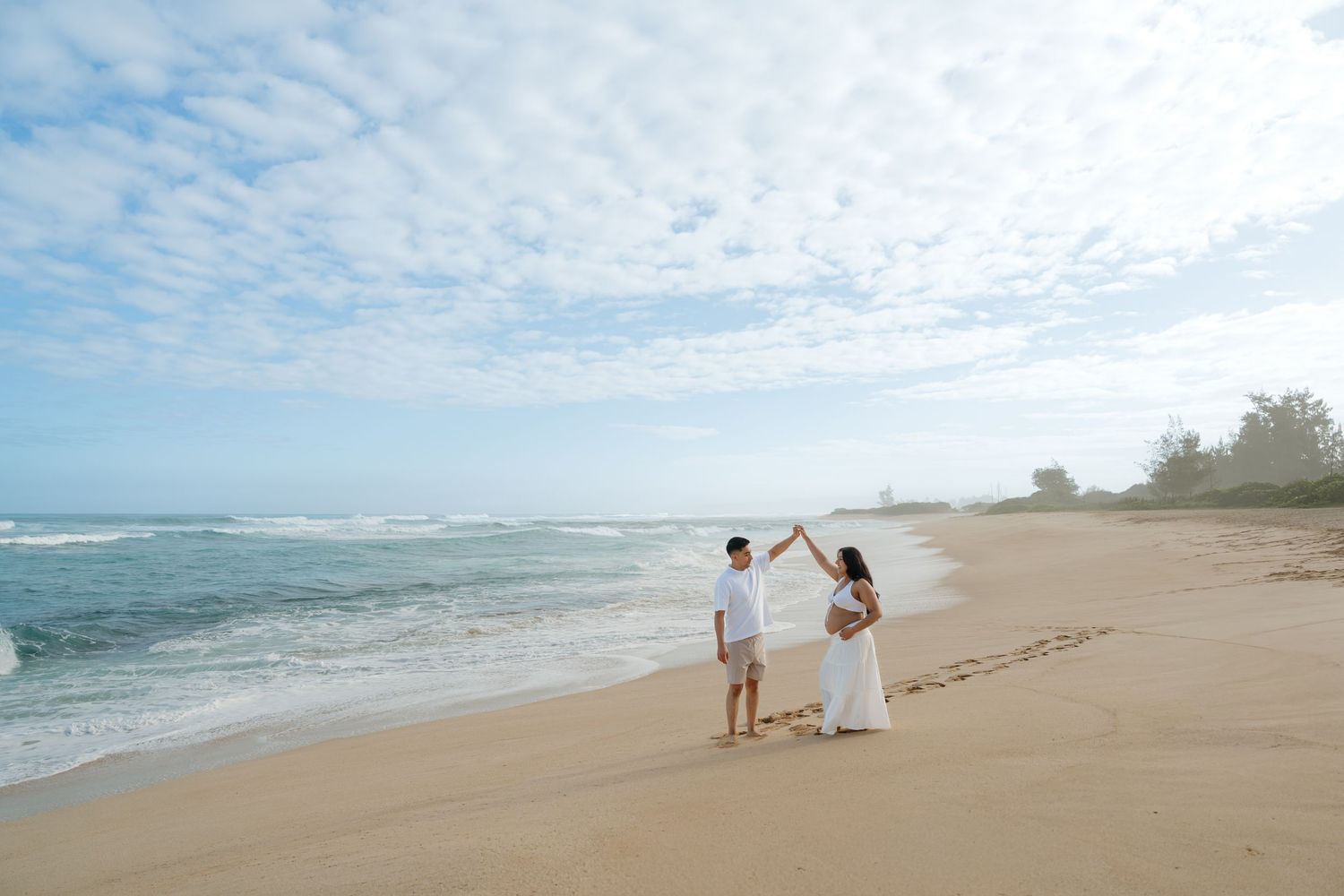 Couple dancing together on a sandy Hawaiian beach with turquoise ocean waves in the background.