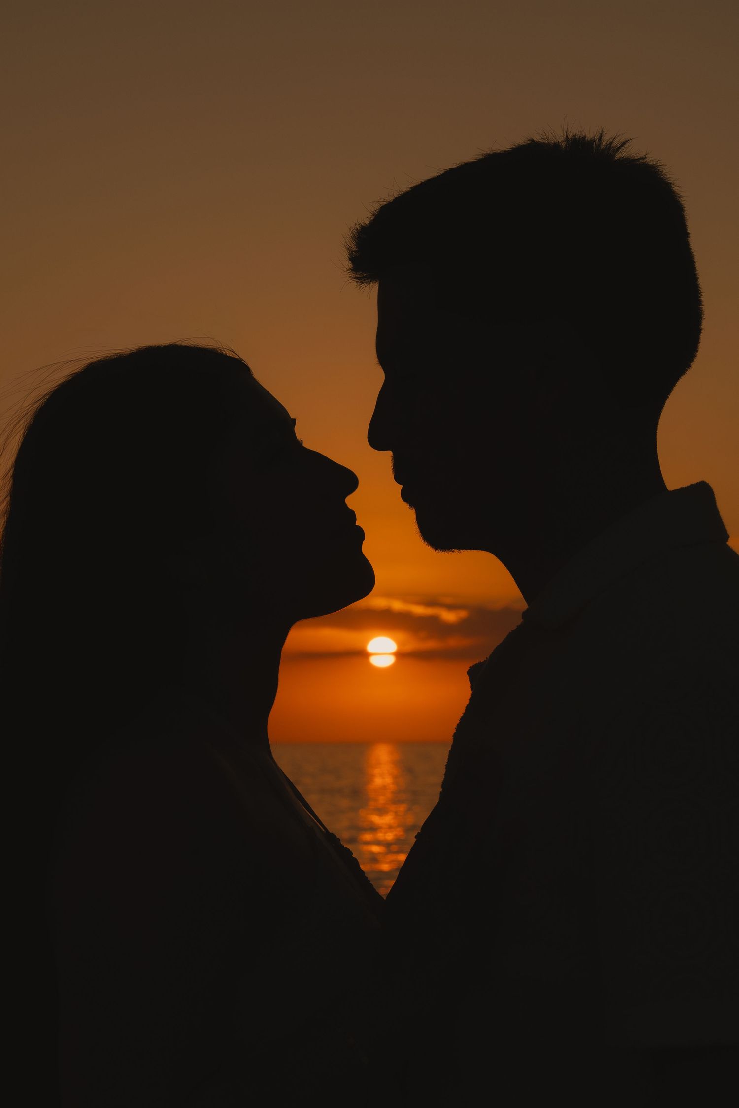 Romantic silhouette of a couple facing each other against a golden ocean sunset backdrop.
