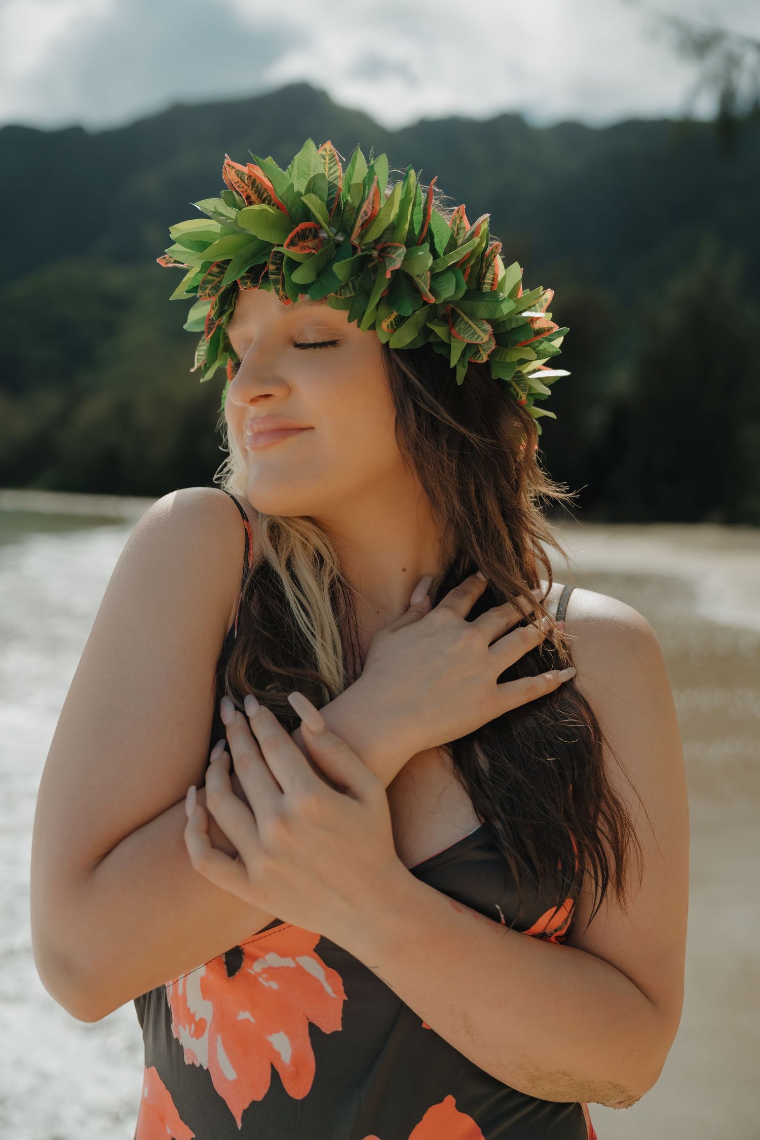 Woman with floral crown and eyes closed, wearing floral swimsuit at tropical beach.