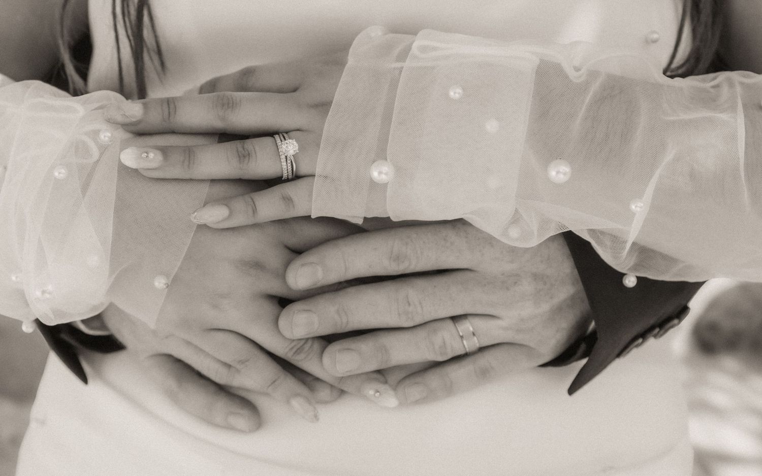 A tender black and white close-up of hands touching through delicate sheer fabric.