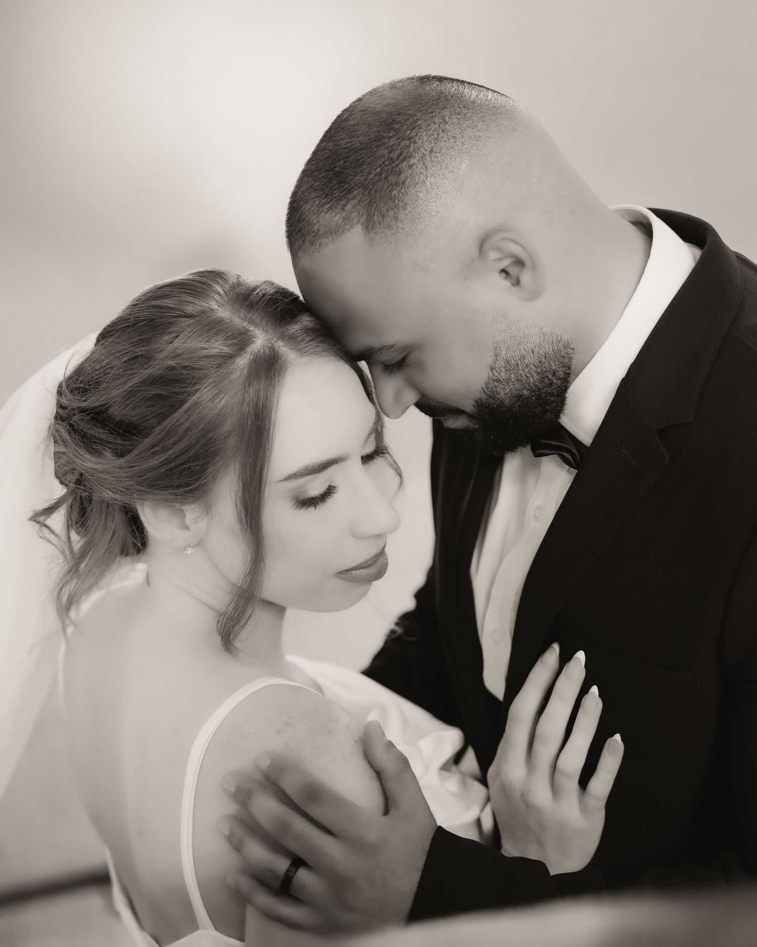 Black and white wedding photo of bride and groom sharing an intimate moment, foreheads touching tenderly.