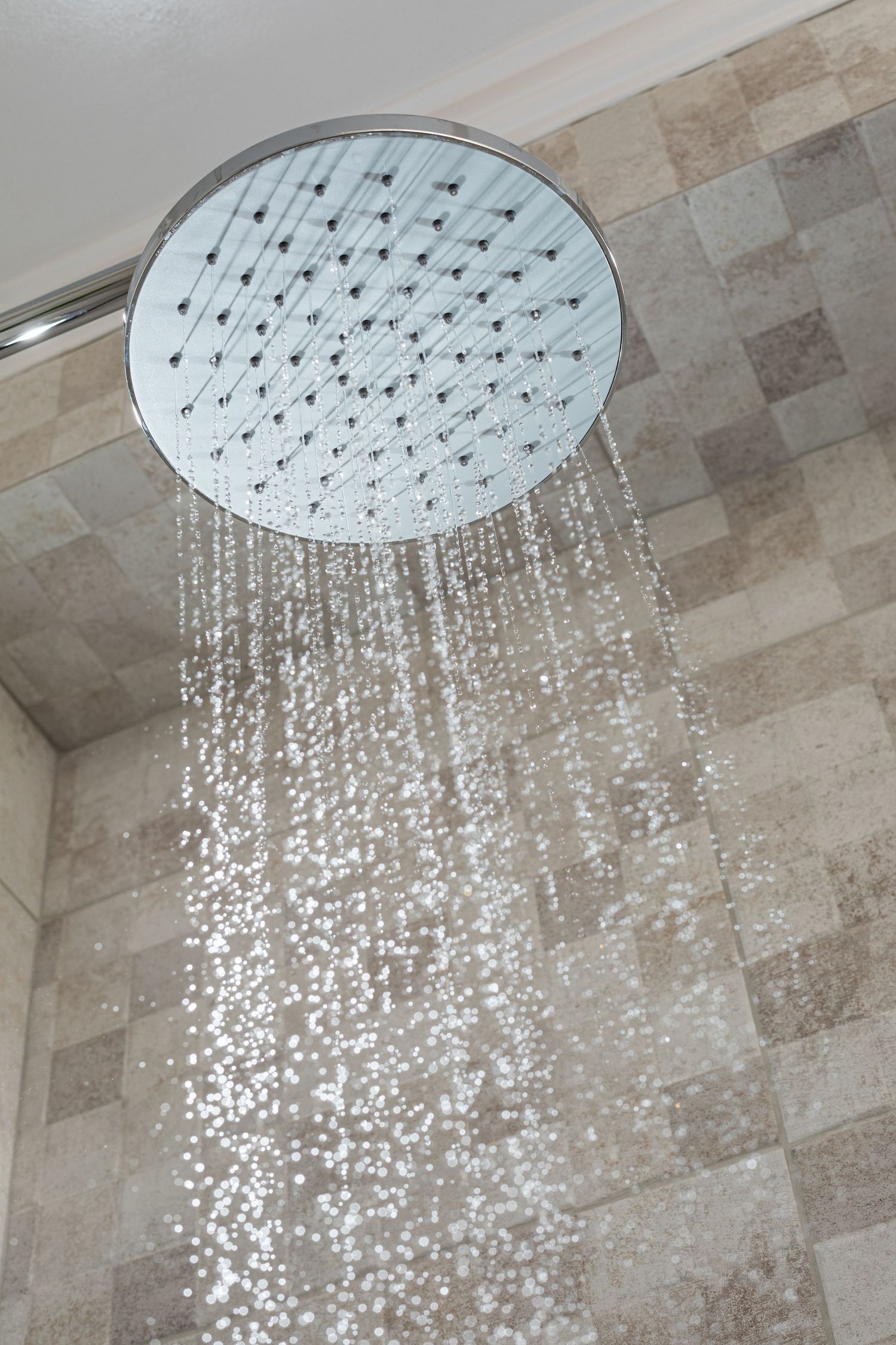 Modern round rainfall showerhead mounted on tiled wall spraying water droplets in a relaxing stream pattern.
