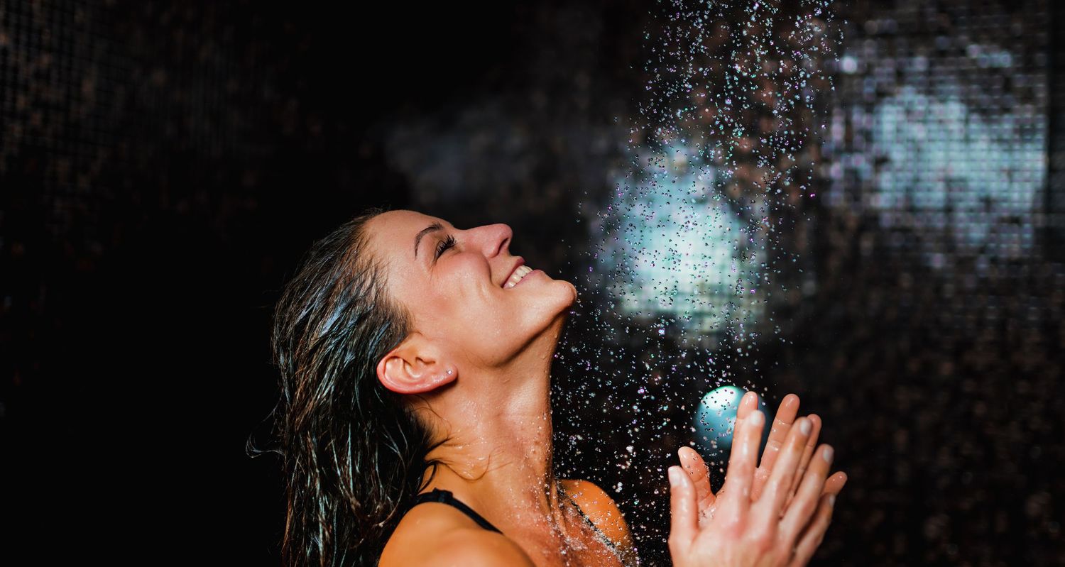 A happy person enjoying a splash of water with a glowing blue light effect in a dark setting.