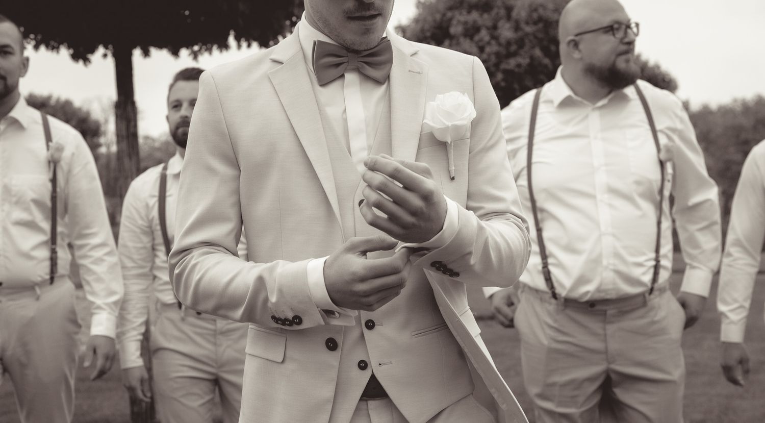 Groomsmen in light colored suits and bow ties gathered together at an outdoor wedding in Germany.